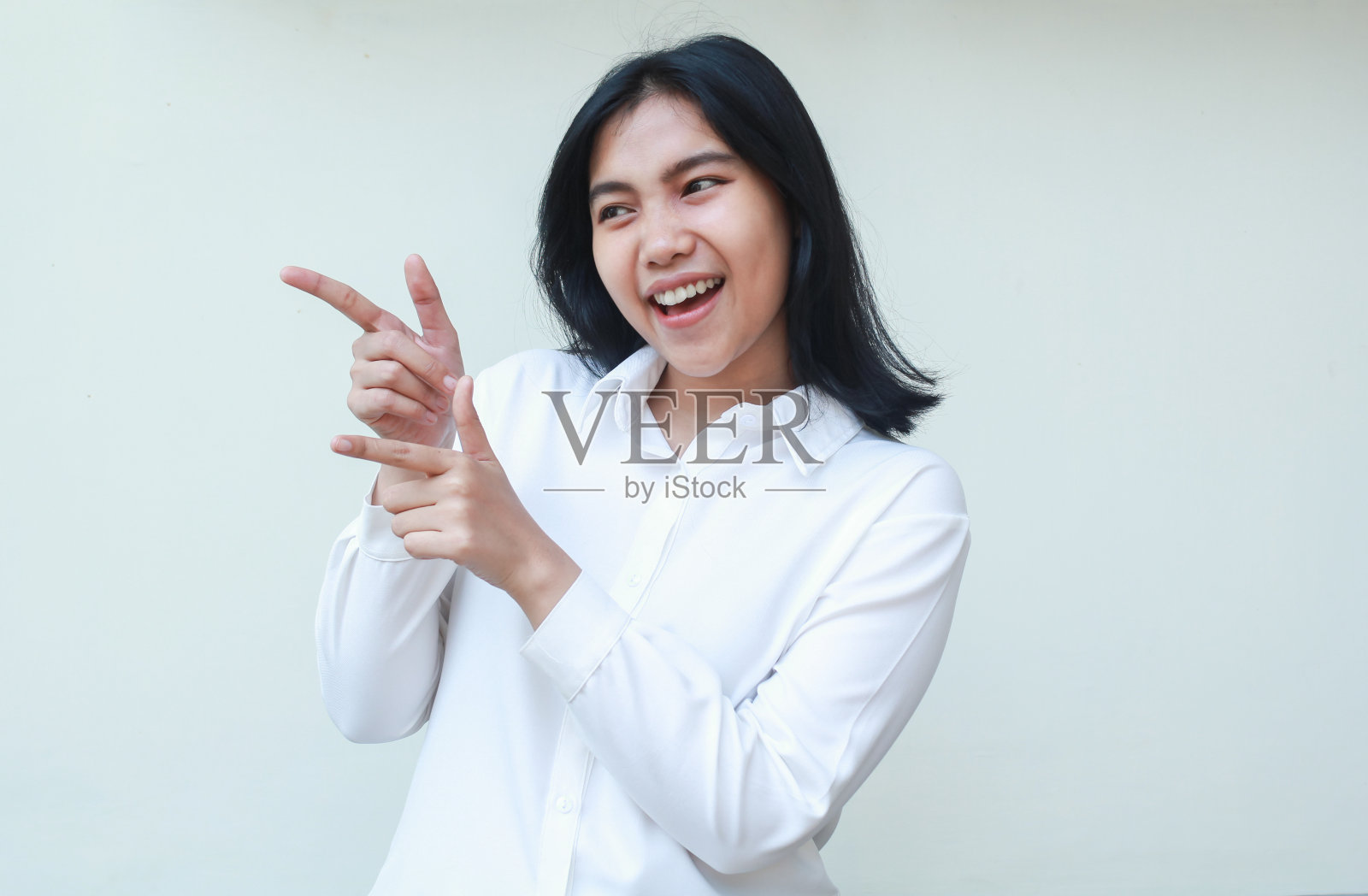 无忧无虑满足的亚洲年轻女商人穿着白色正装衬衫，手指向一边的空地望着别处，兴奋的员工展示着促销活动，孤立在白色的背景中照片摄影图片