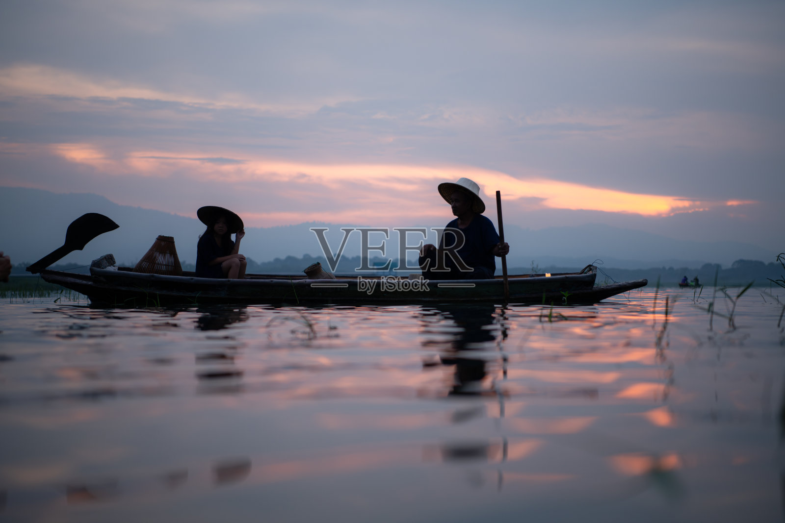 日出时渔夫的剪影，站在划艇上撒网捕鱼照片摄影图片
