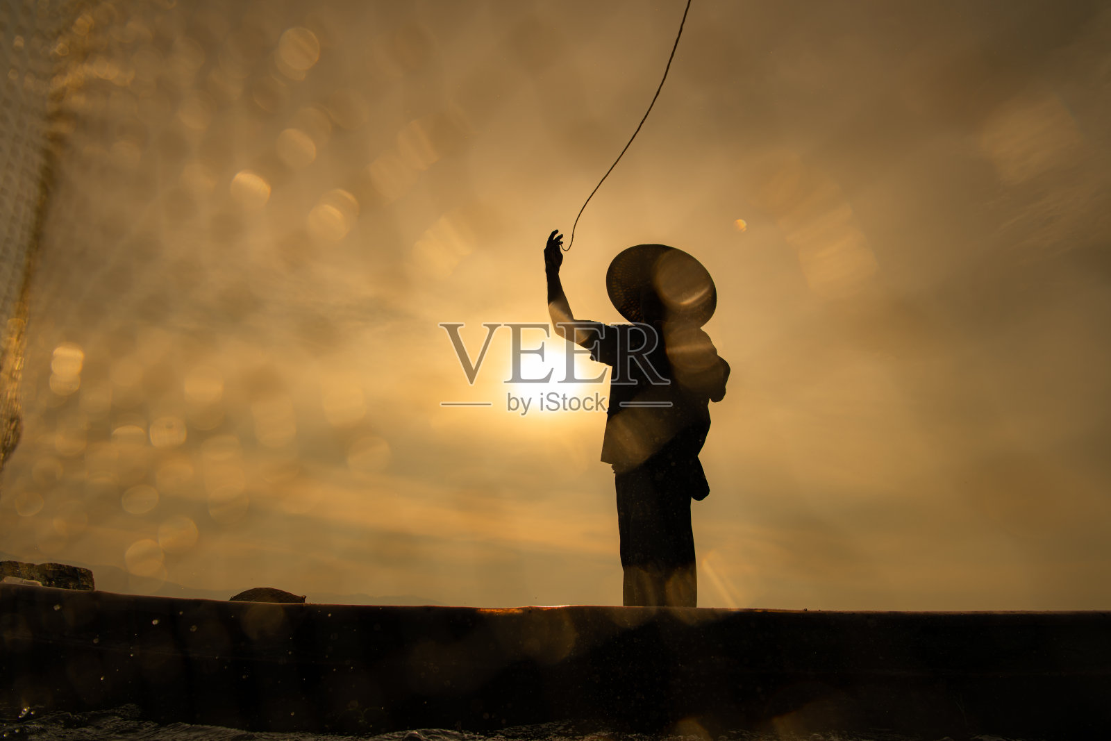 日出时渔夫的剪影，站在划艇上撒网捕鱼照片摄影图片
