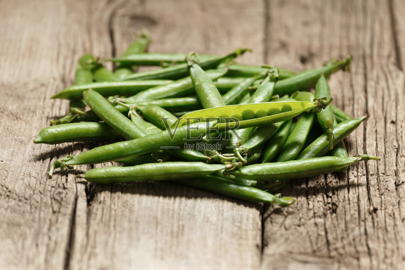 在木制背景上，新鲜的绿色豌豆在封闭和开放的豆荚中。照片摄影图片
