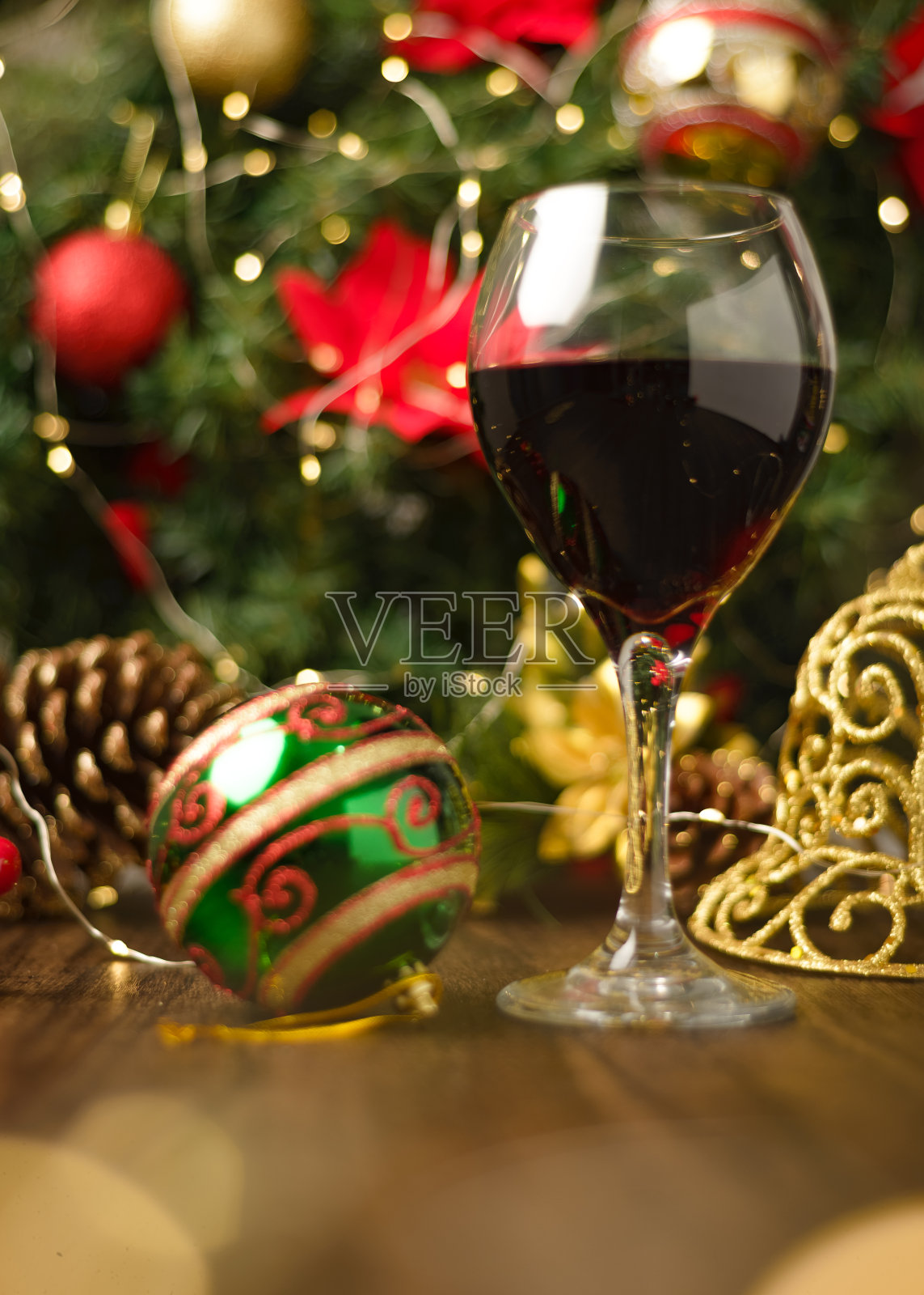 圣诞装饰的木桌上的一杯红酒。背景是圣诞树和彩灯。照片摄影图片