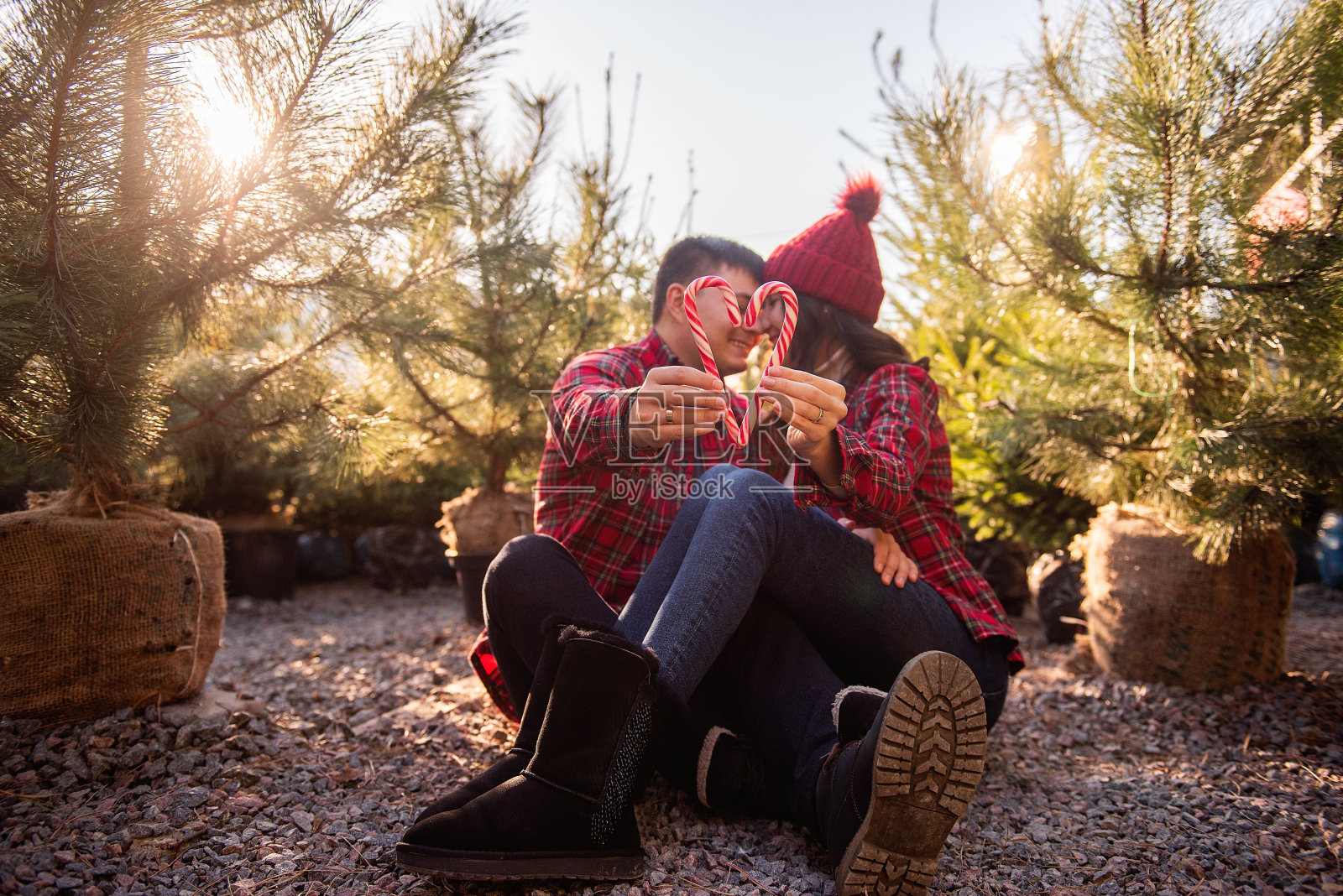 身穿格子衬衫、头戴针织帽、手拿心形拐杖糖的热恋情侣照片摄影图片
