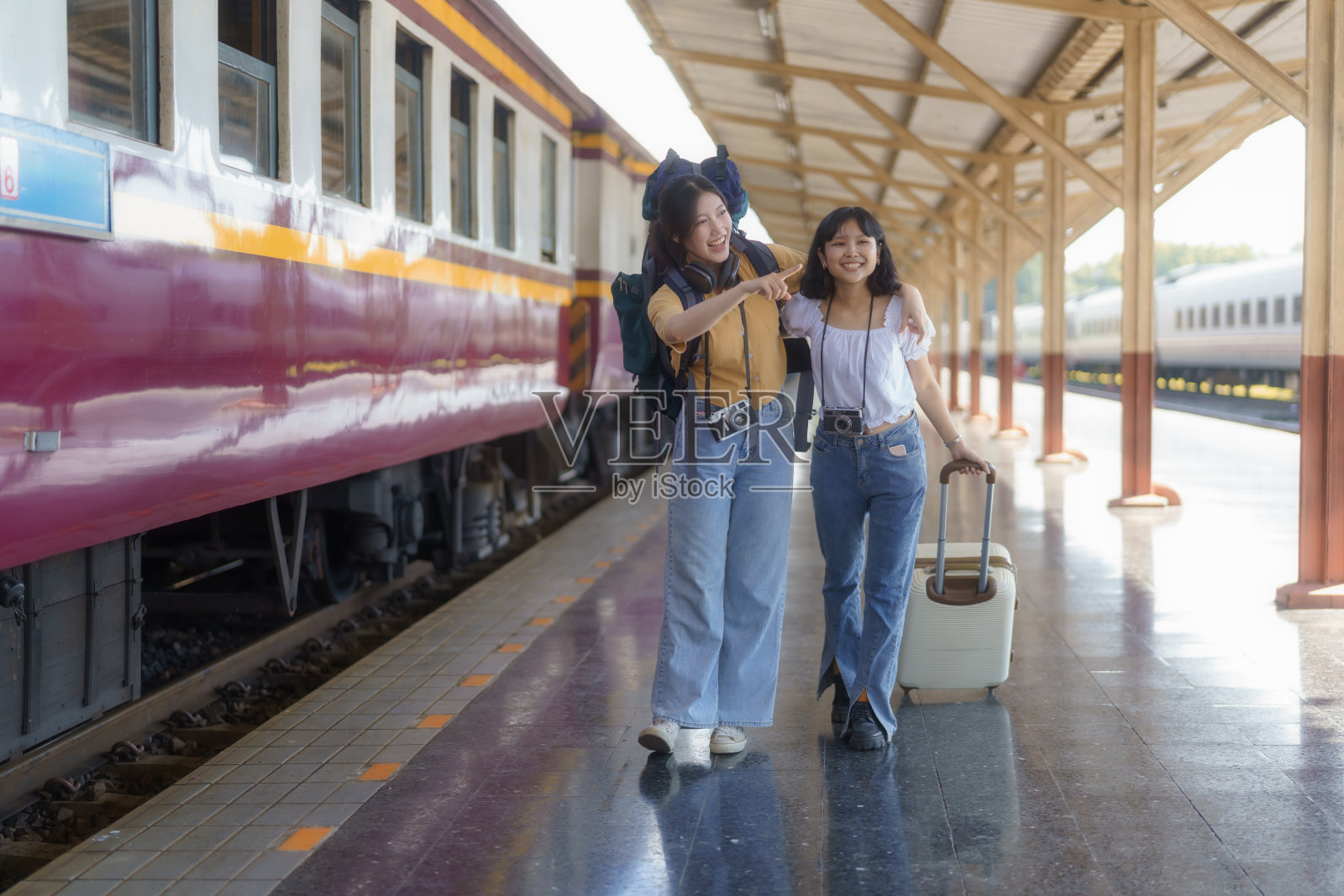 两个年轻的亚洲女性在铁路上背着背包旅行者，在火车站背着背包旅行者，旅行概念。走在火车站的女游客。照片摄影图片