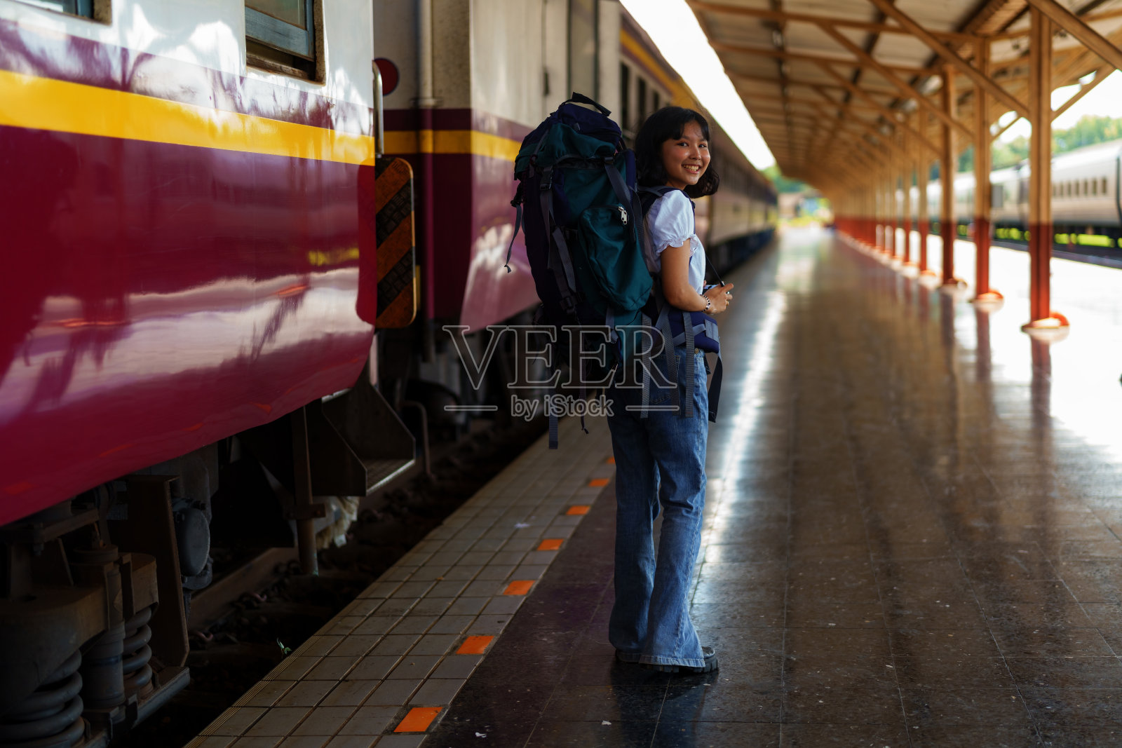 年轻的亚洲女旅行者在火车上背着双肩包，在火车站背着双肩包和帽子，旅行概念。走在火车站的女游客。照片摄影图片