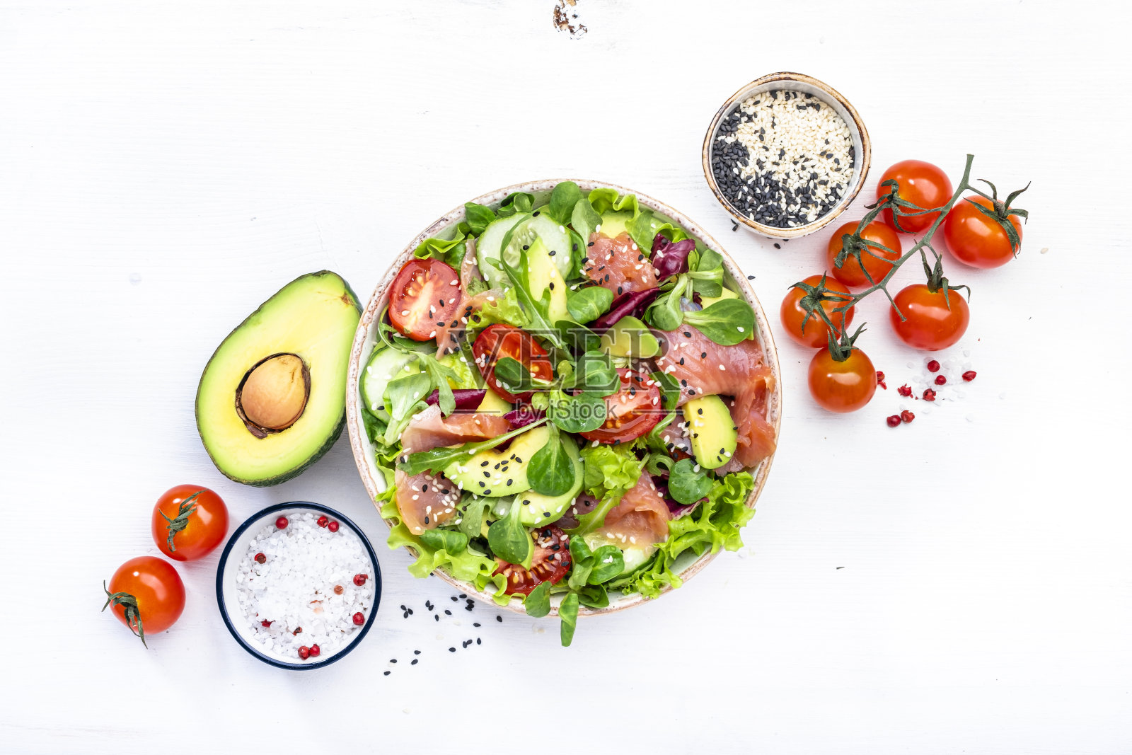 生酮沙拉，加盐三文鱼，鳄梨，番茄，生菜，黄瓜，芝麻。富含健康脂肪的低碳水化合物早餐。白色桌面背景，俯视图照片摄影图片