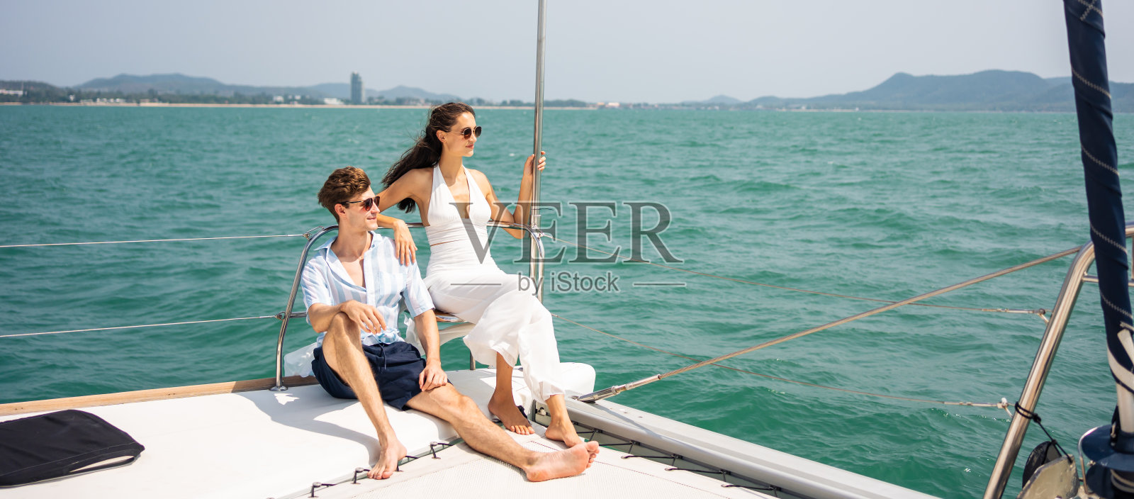 一对浪漫的高加索夫妇在游艇上欣赏美丽的景色。迷人的年轻男女在夏日夕阳下的双体船中一起庆祝蜜月旅行照片摄影图片