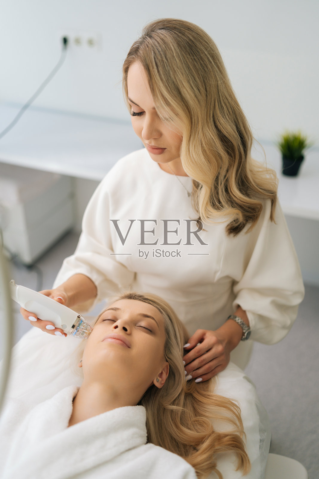 在拉皮过程中，金发女客户闭着眼睛躺着接受刺激的美容面部治疗的垂直肖像。照片摄影图片