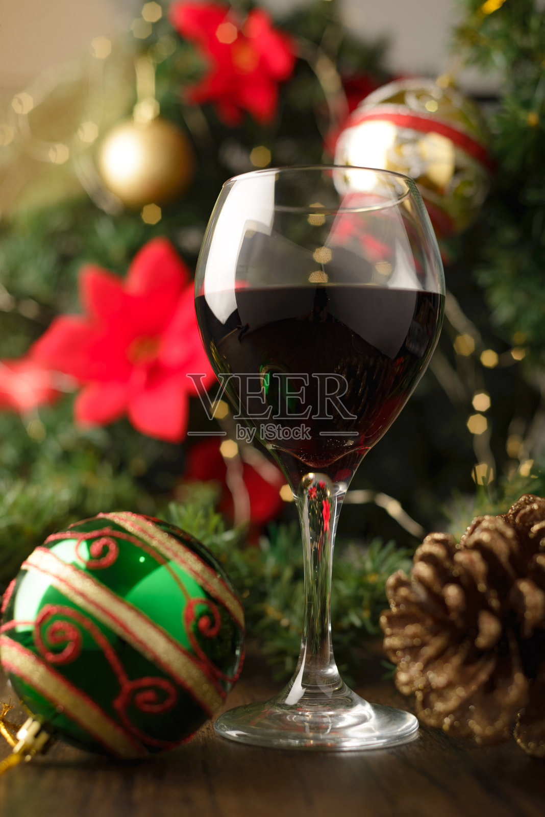 圣诞装饰的木桌上的一杯红酒。背景是圣诞树和彩灯。照片摄影图片