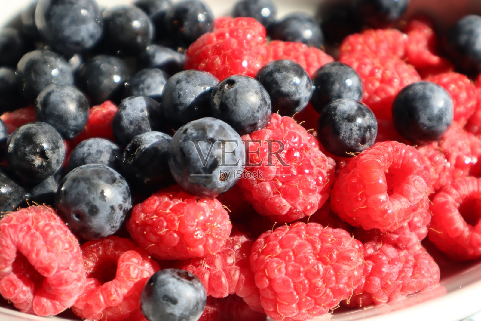 白色盘子上有覆盆子和蓝莓，背景是白色的照片摄影图片