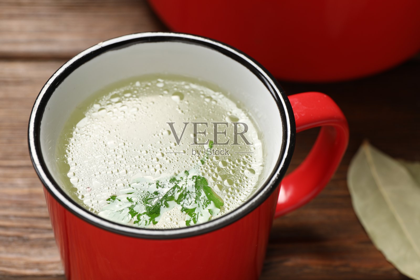 木桌上的红杯子里放着美味的清汤，特写照片摄影图片