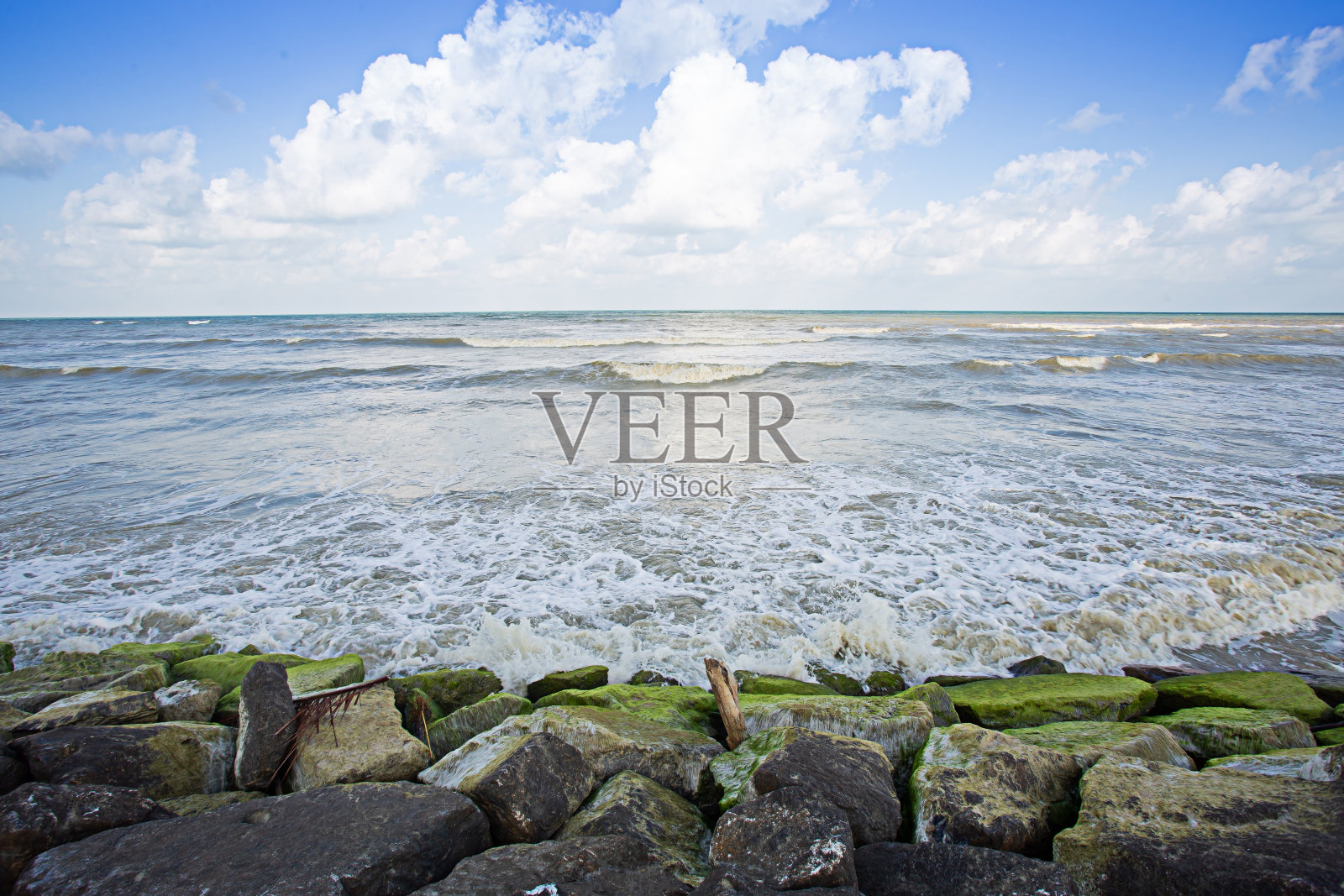 在一个晴朗的日子里，海浪冲击着海滩上的岩石。照片摄影图片