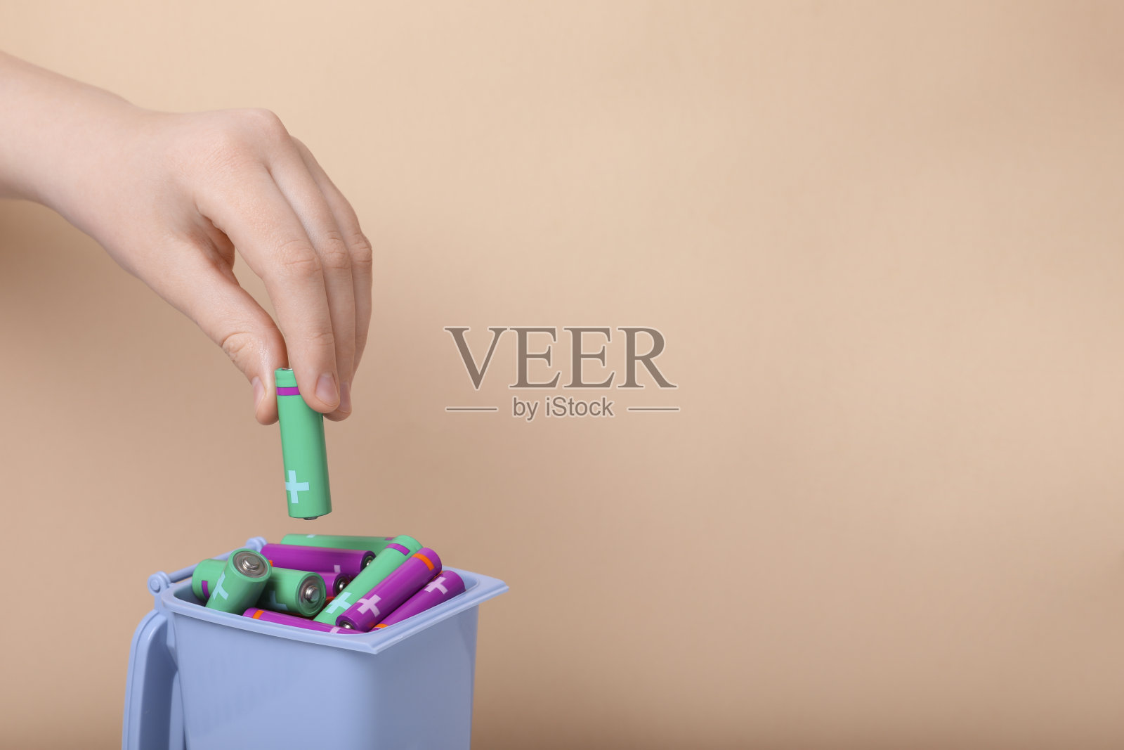 一个女人把用过的AA号电池放进回收箱，米色背景，特写。文本空间照片摄影图片