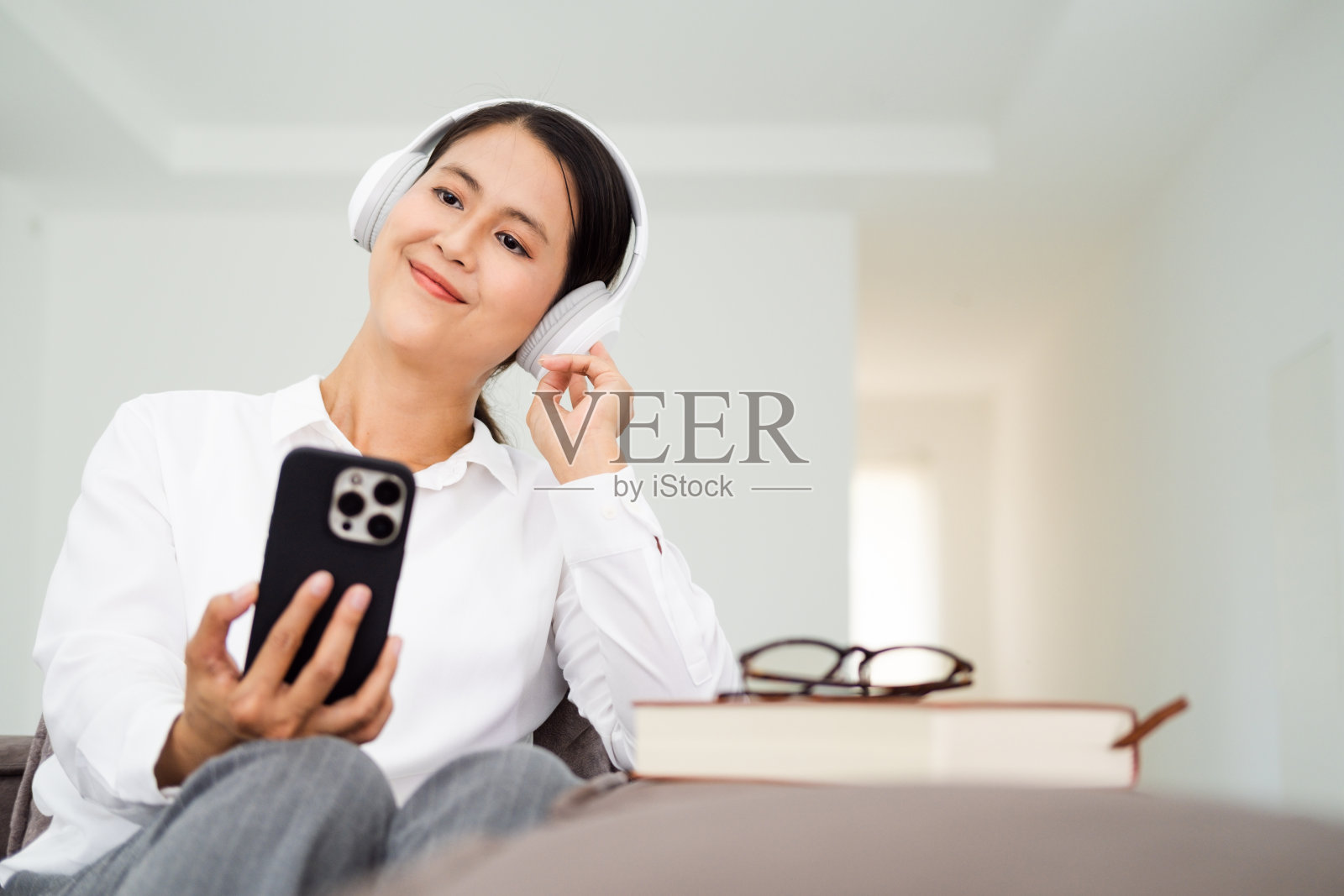 成熟的亚洲中年妇女下班后在家里的沙发沙发上放松，戴着耳机听音乐广播播客电子书照片摄影图片