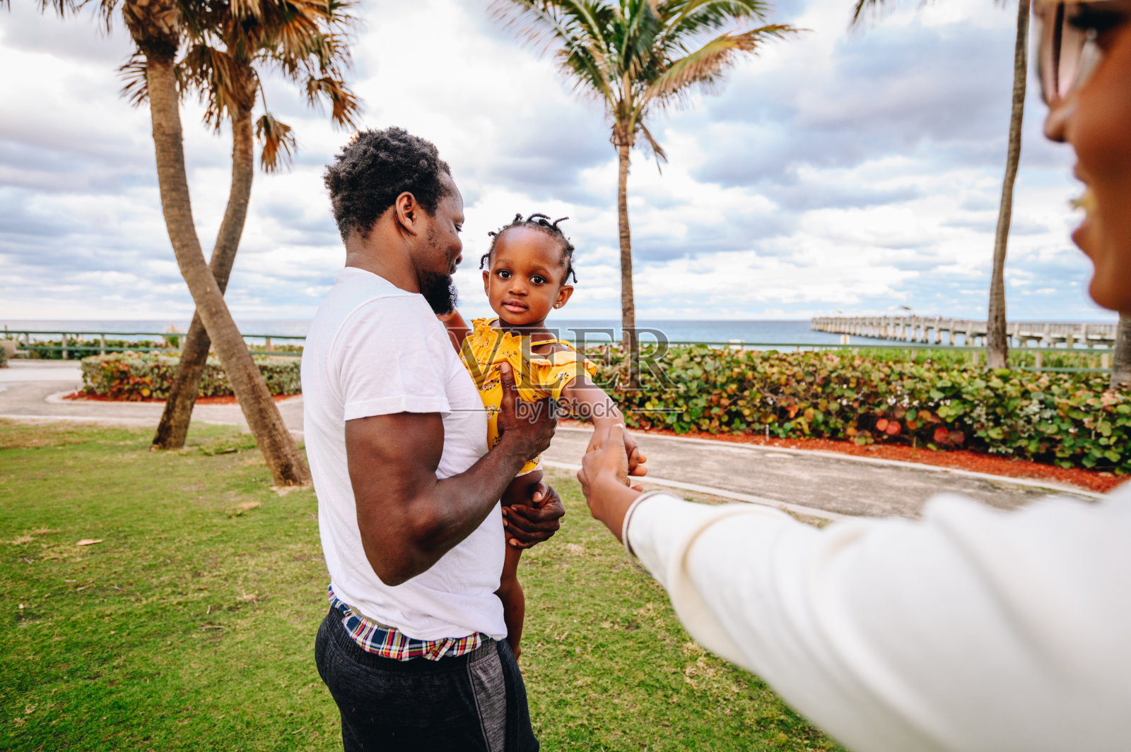 非洲裔美国父亲和母亲在热带地区与可爱的蹒跚学步的女儿玩耍，家庭度假和现代男子气概照片摄影图片