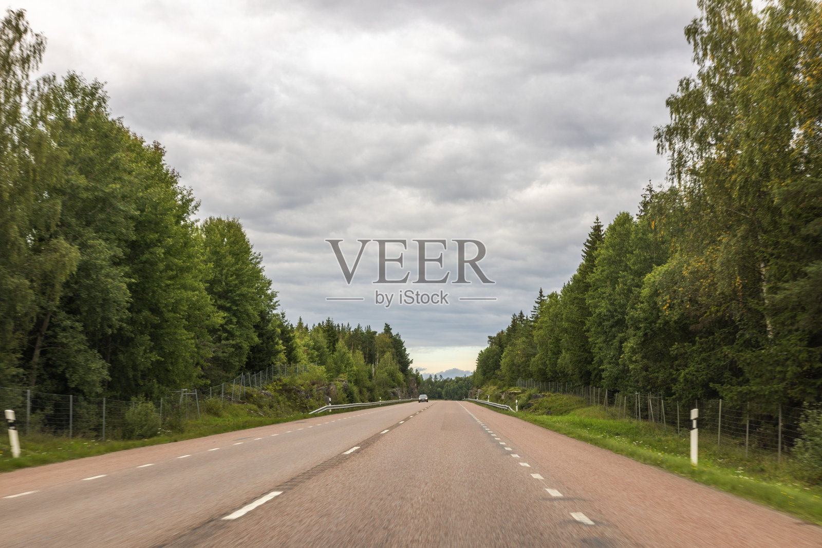 公路上孤零零的汽车的美丽景色，两边都是高大的绿树。道路延伸到远处，与地平线上多云的天空融为一体。瑞典。照片摄影图片