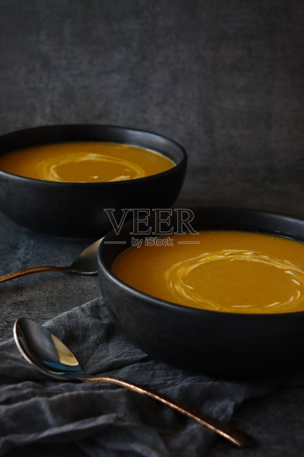 一碗自制的万圣节南瓜汤，上面点缀着漩涡状的酸奶，金属勺子，深灰色的薄纱，斑驳的灰黑色背景，高架视图，聚焦于前景照片摄影图片