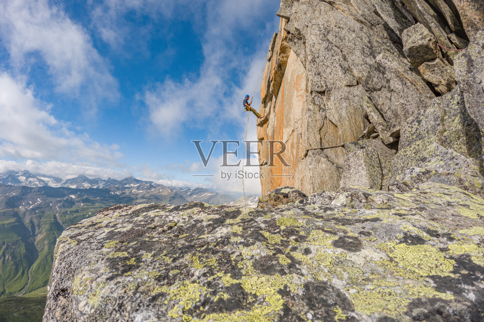 男人从山上的悬崖上沿绳索下降照片摄影图片