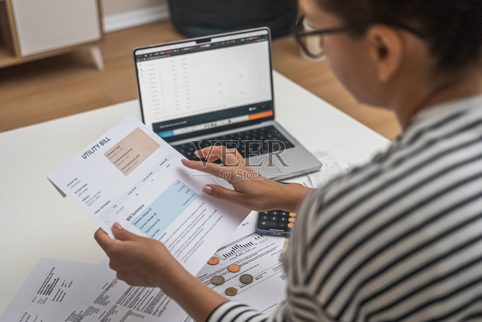 一名妇女拿着笔记本电脑在桌子旁查看水电费账单和税务信息，准备付款。照片摄影图片
