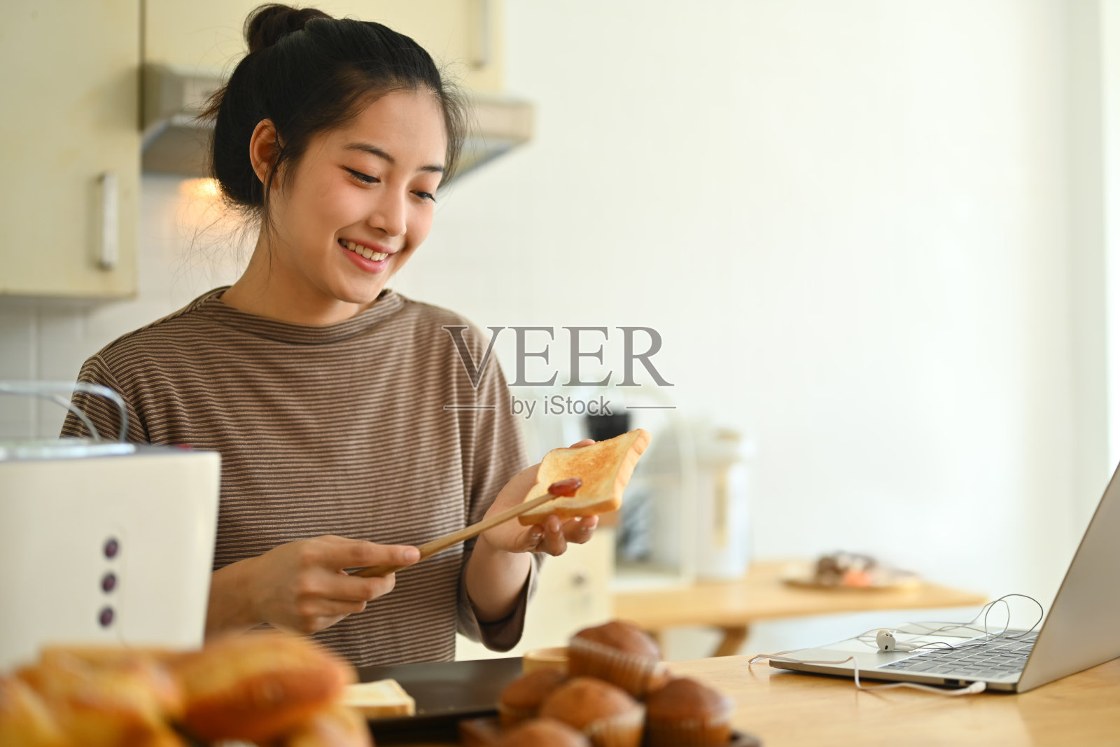 年轻迷人的家庭主妇在厨房准备早餐时把草莓酱涂在面包片上照片摄影图片