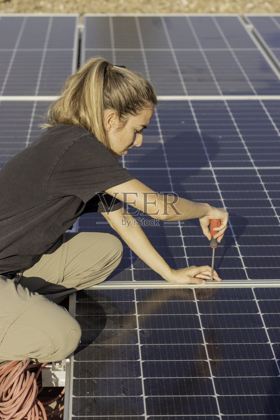 俯视图，年轻女子拧螺丝组装屋顶上的光伏太阳能板照片摄影图片