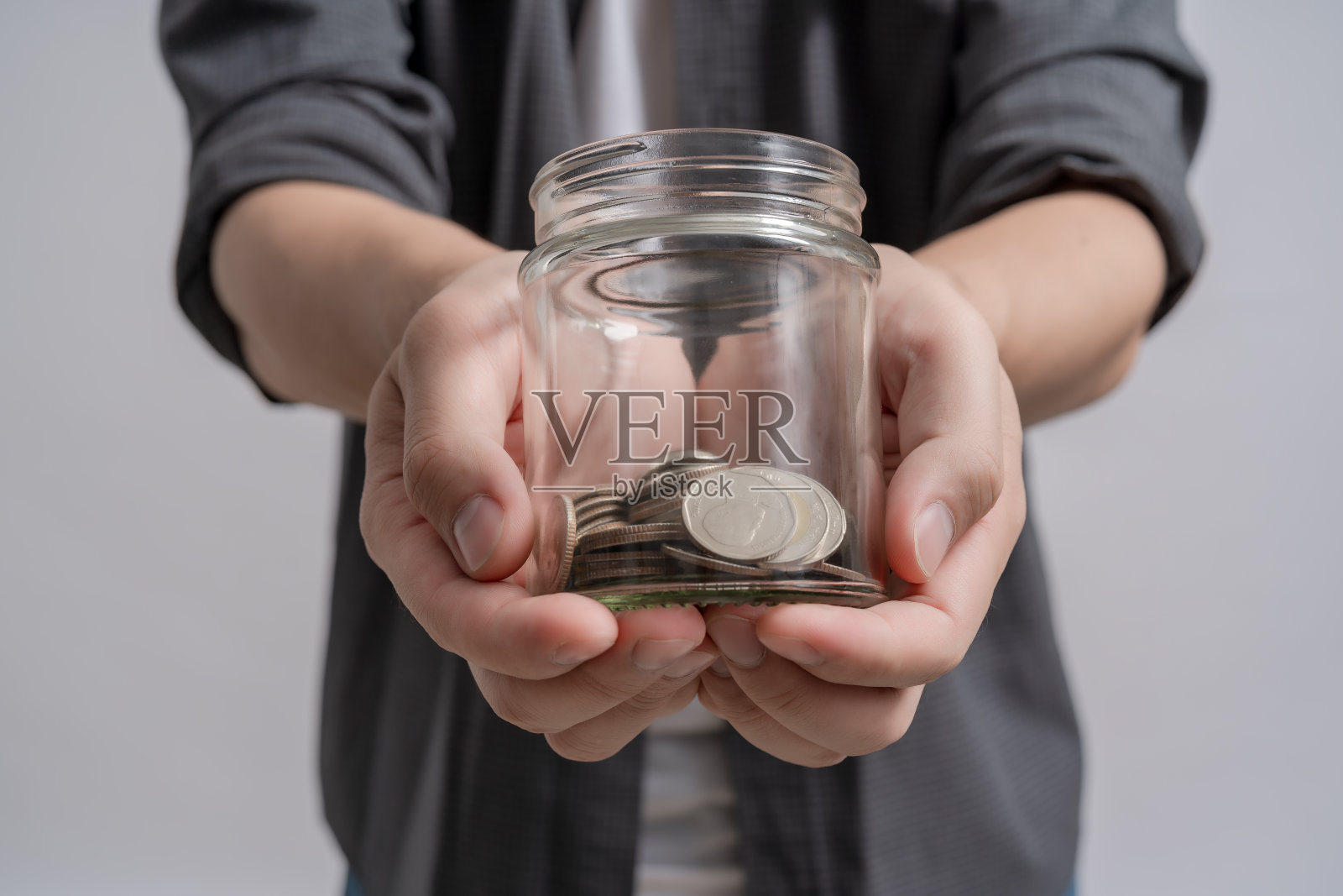 手里拿着一个玻璃罐子，里面有很多硬币，为了省钱。照片摄影图片