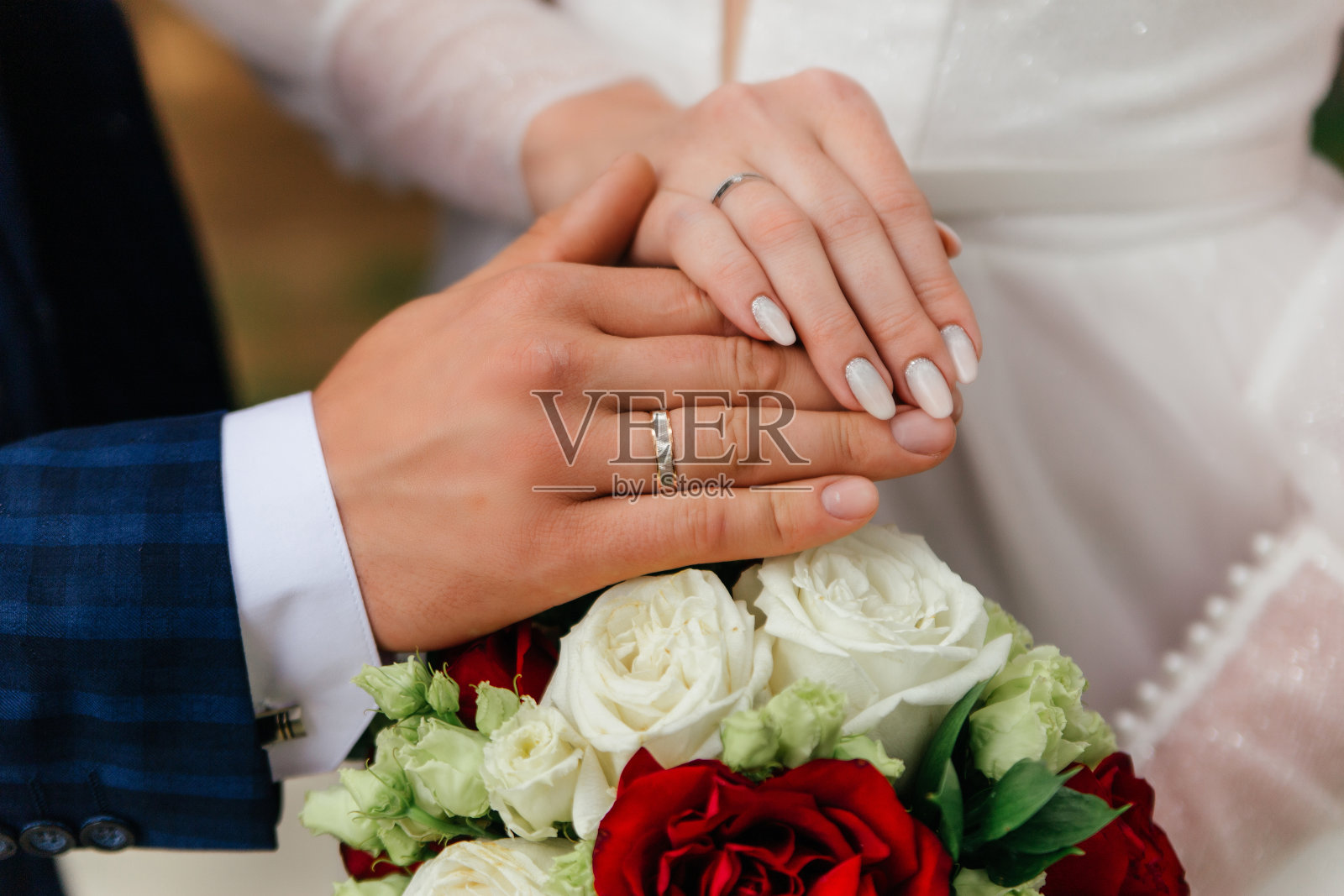 新娘和新郎的手戴着戒指，背景是婚礼的玫瑰花束。婚姻的概念照片摄影图片