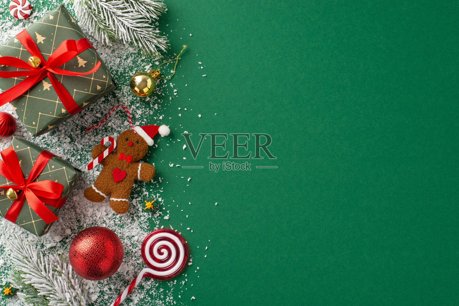 创新的新年主题灵感。顶视图，翠绿的礼盒上装饰着蝴蝶结，红色，金色的小饰物，姜饼人玩具，棒棒糖，雪白的绿色表面上结霜的冷杉树枝，问候的空间照片摄影图片