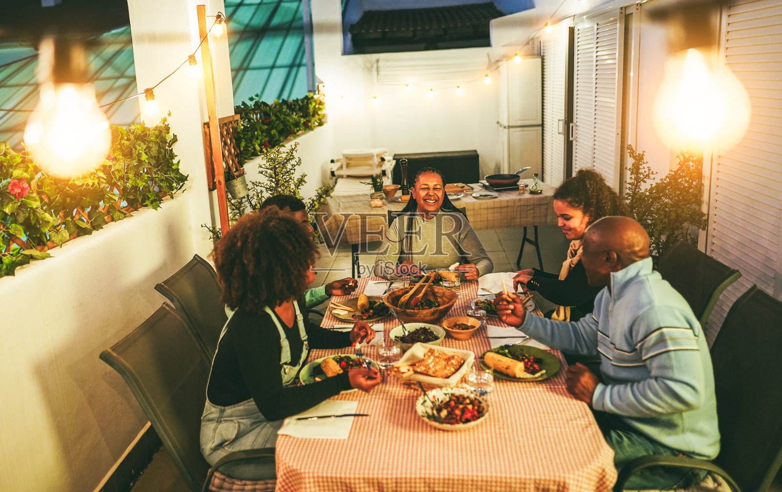 快乐的非裔美国家庭在户外露台上一起吃晚餐-假日生活方式概念-温柔地关注母亲的脸照片摄影图片