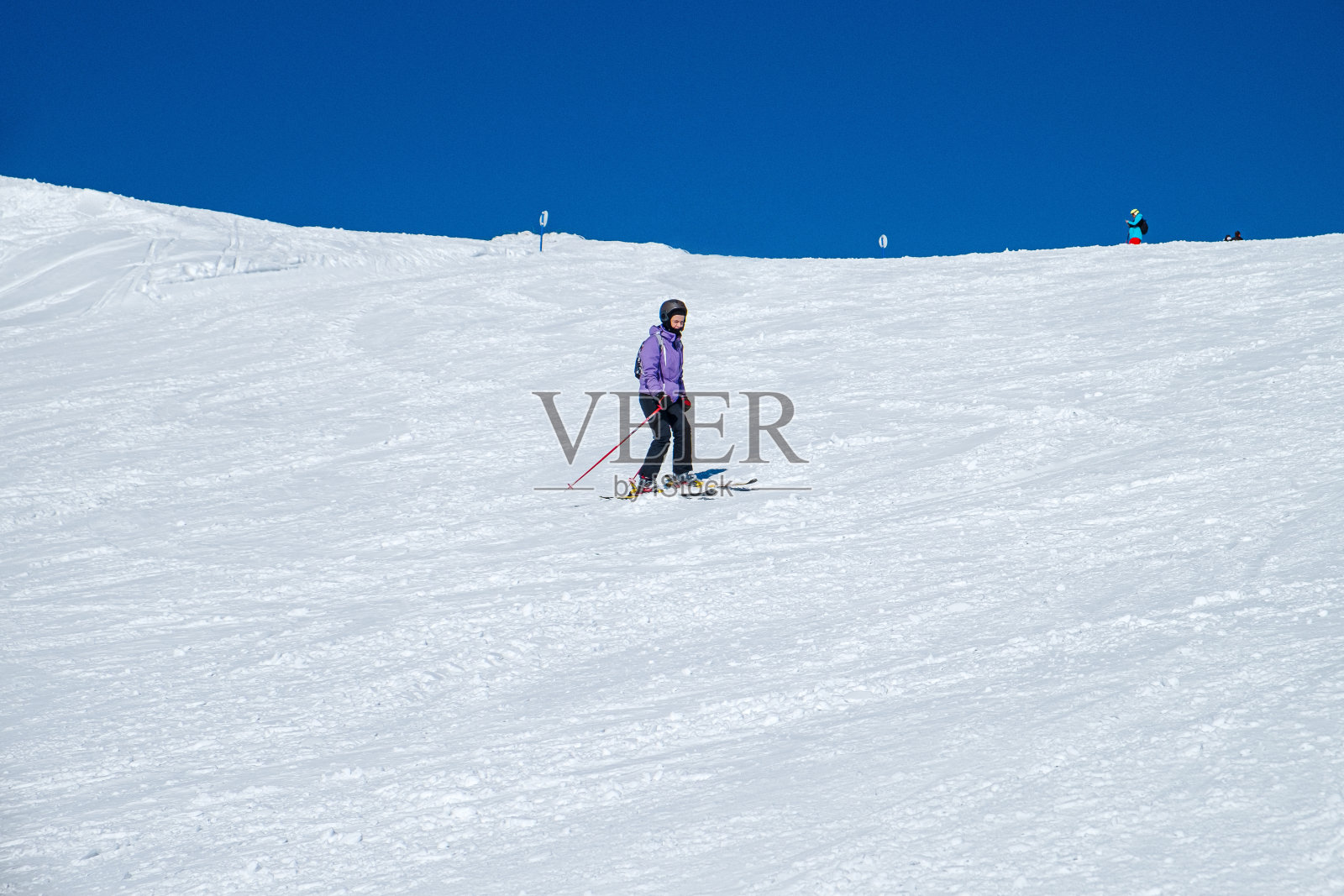 在一个晴朗的日子里，穿着滑雪服慢慢下坡，斜坡上覆盖着皑皑白雪照片摄影图片