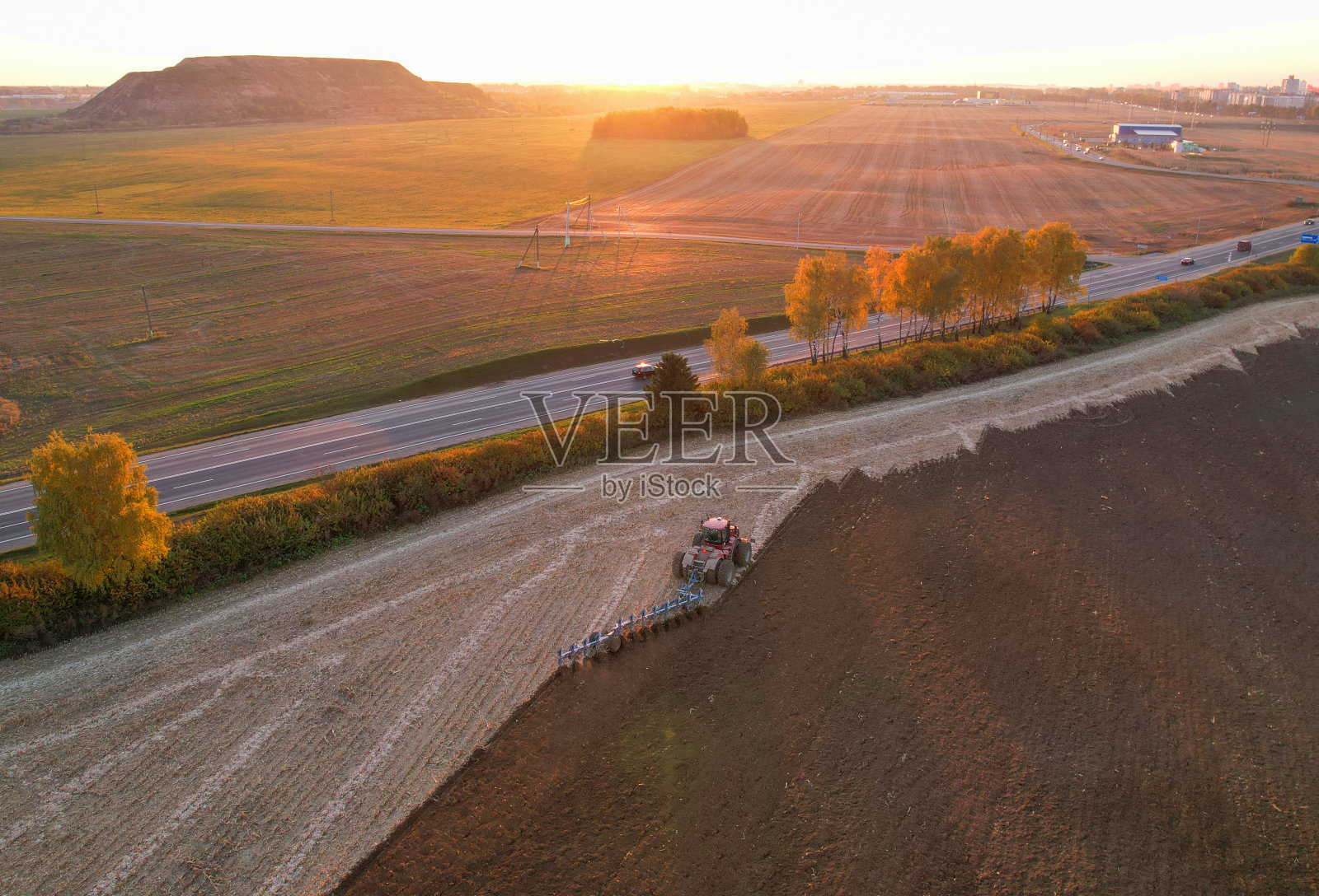 日落时分，拖拉机在犁地。照片摄影图片