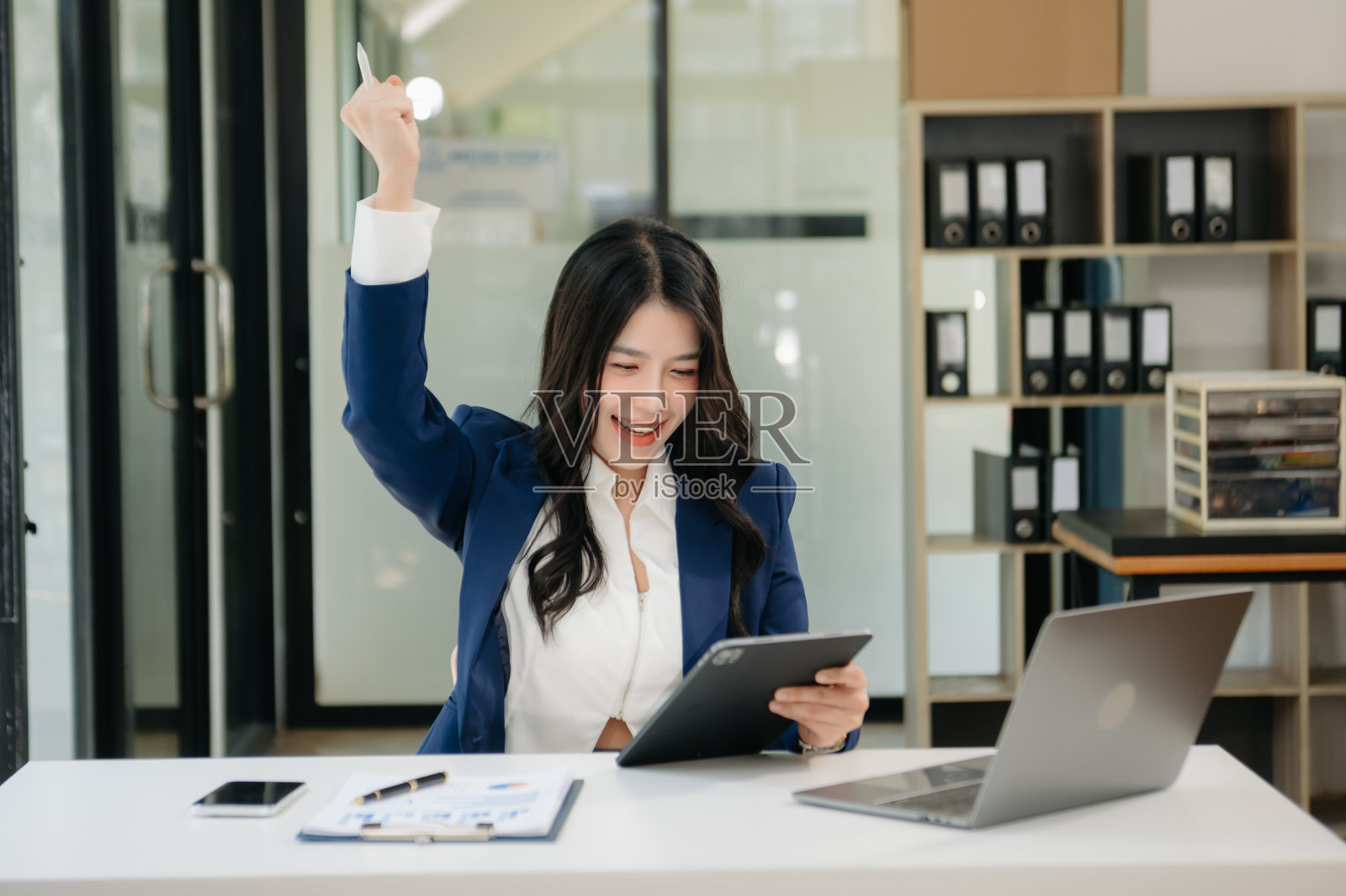 亚洲女商人对她们在办公室用平板电脑、笔记本电脑和做笔记所做的工作感到高兴和快乐。照片摄影图片