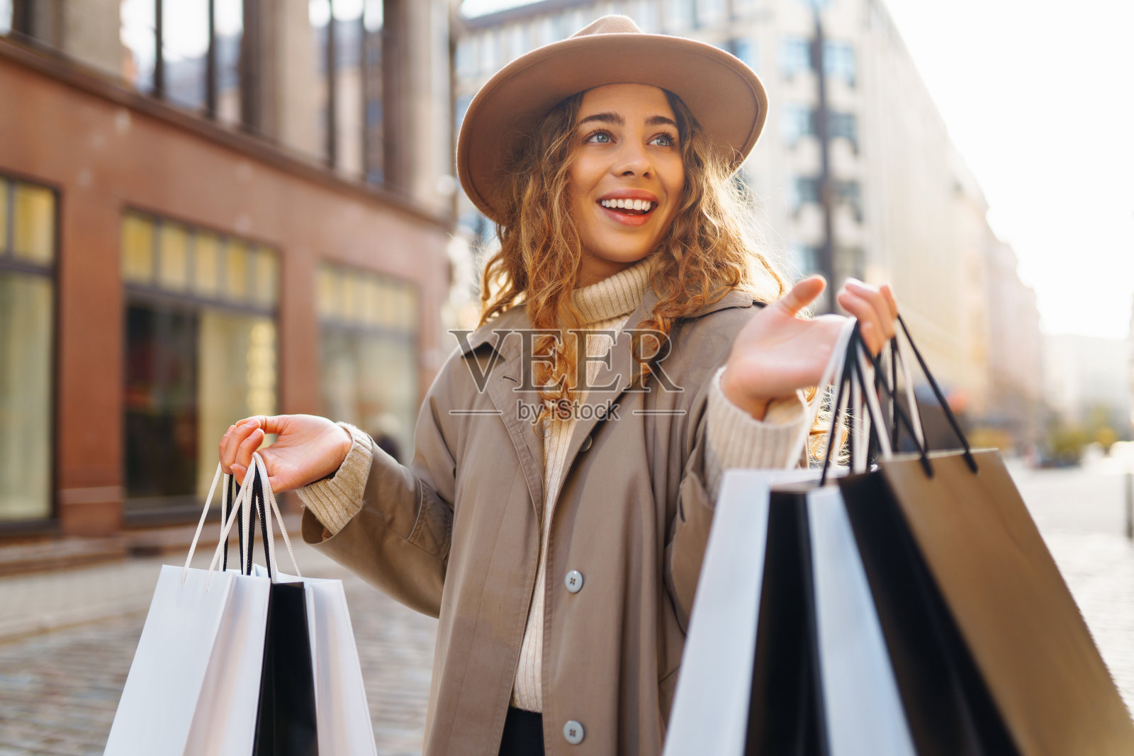 一位穿着大衣、戴着帽子、提着购物袋的时尚女子走过一家购物中心。照片摄影图片