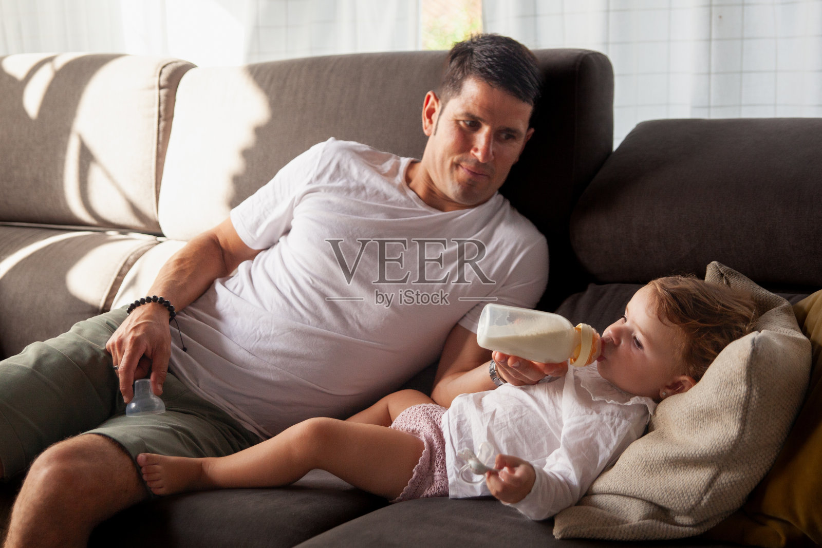 年轻的父亲慈爱地用奶瓶喂他的婴儿照片摄影图片