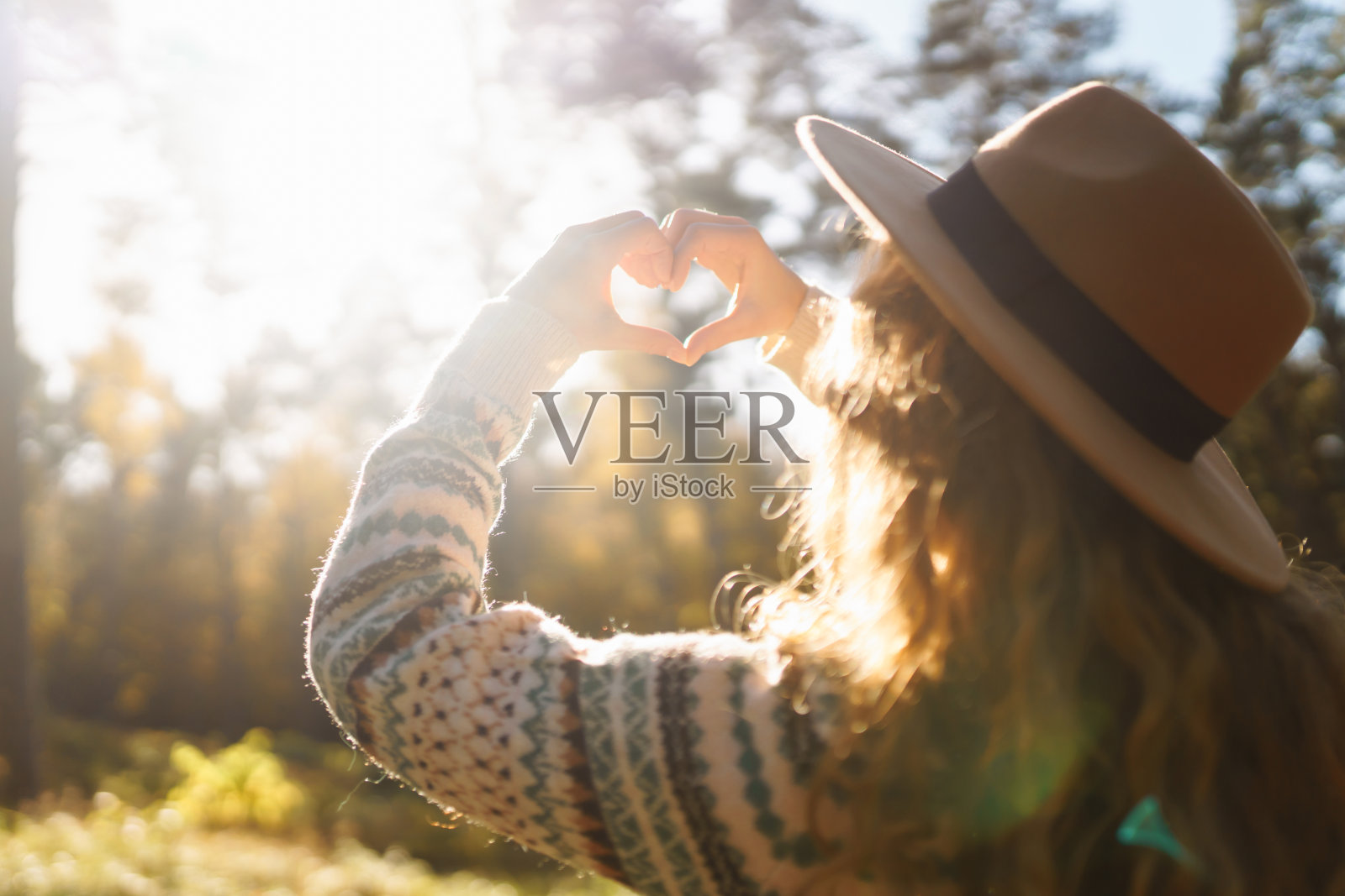 戴着帽子、穿着毛衣的年轻女子双手握成心形。照片摄影图片