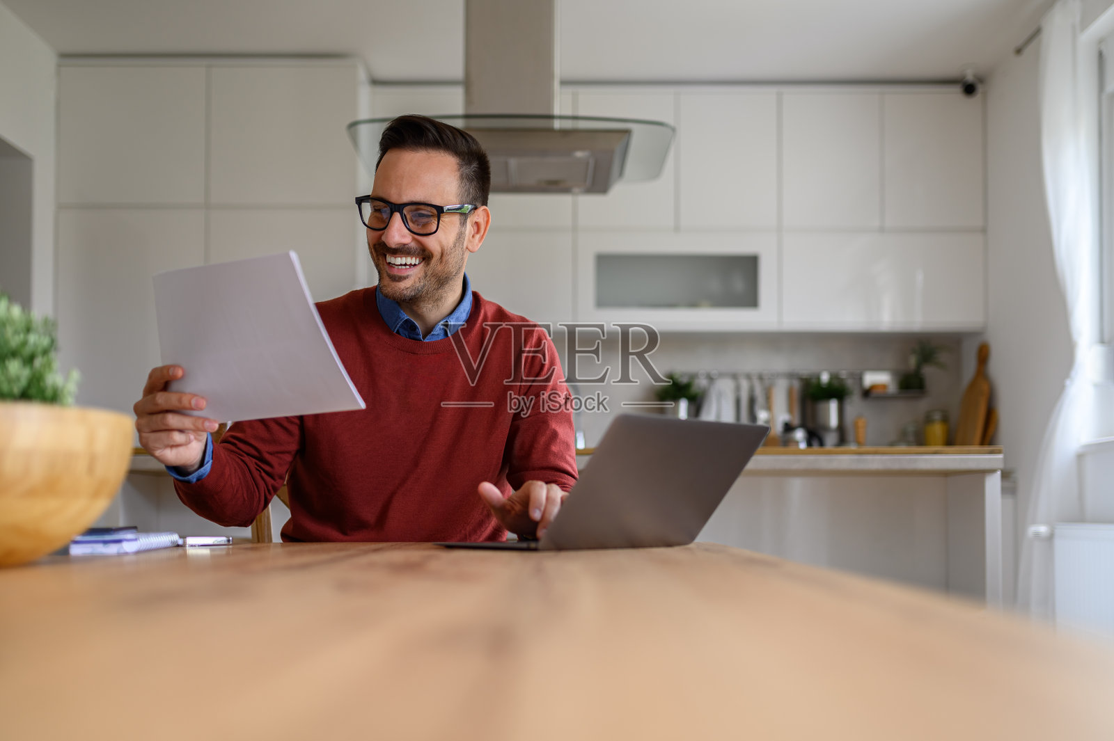 微笑的商人阅读财务文件，在办公桌上使用笔记本电脑，而在家工作照片摄影图片