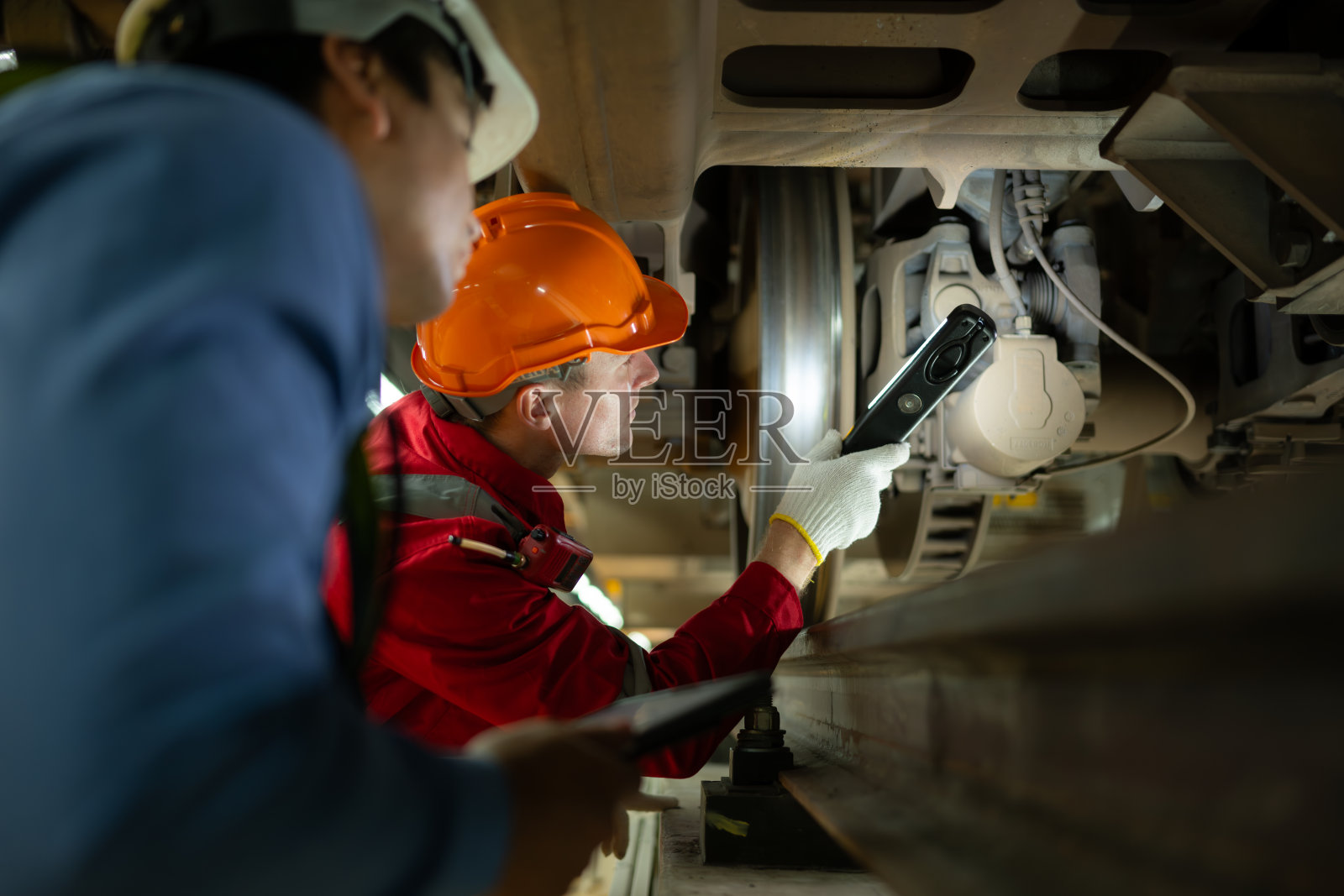 两名电动列车工程师在发现电动列车的机械故障后，使用探照灯定位和检查损坏的部分。在电动火车修理厂照片摄影图片