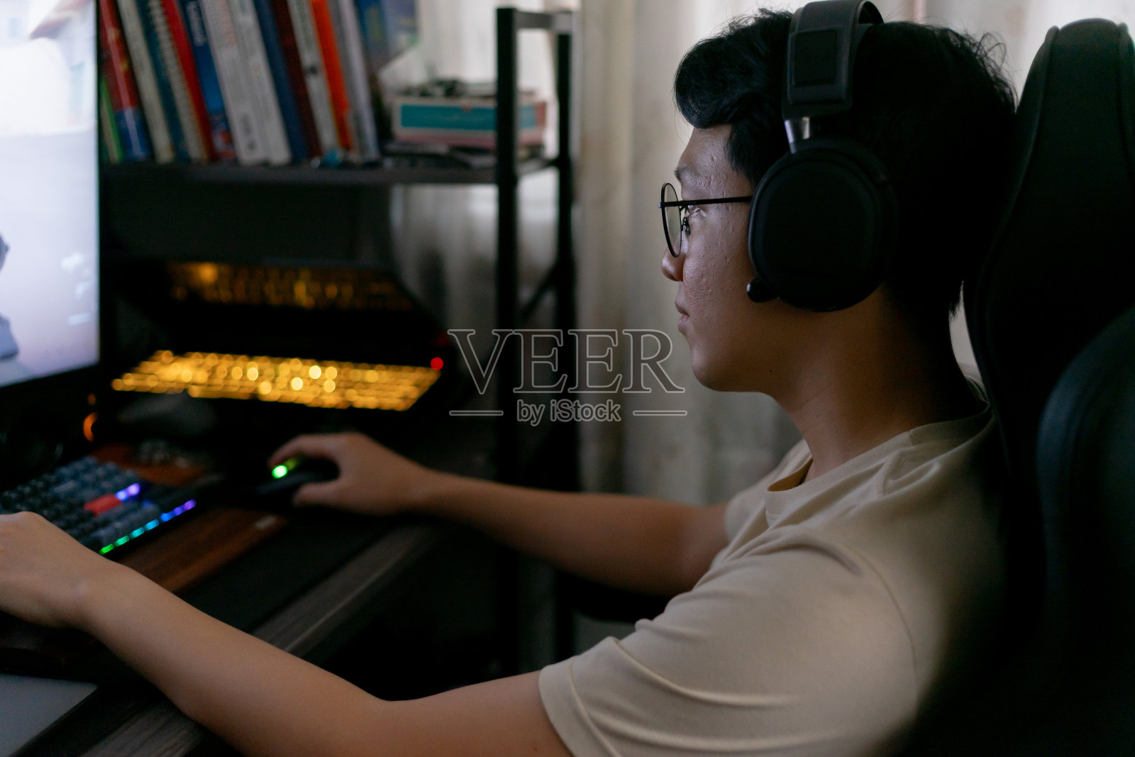 亚洲年轻玩家戴着耳机专心玩电脑游戏。乐趣和娱乐爱好技术在游戏室。照片摄影图片