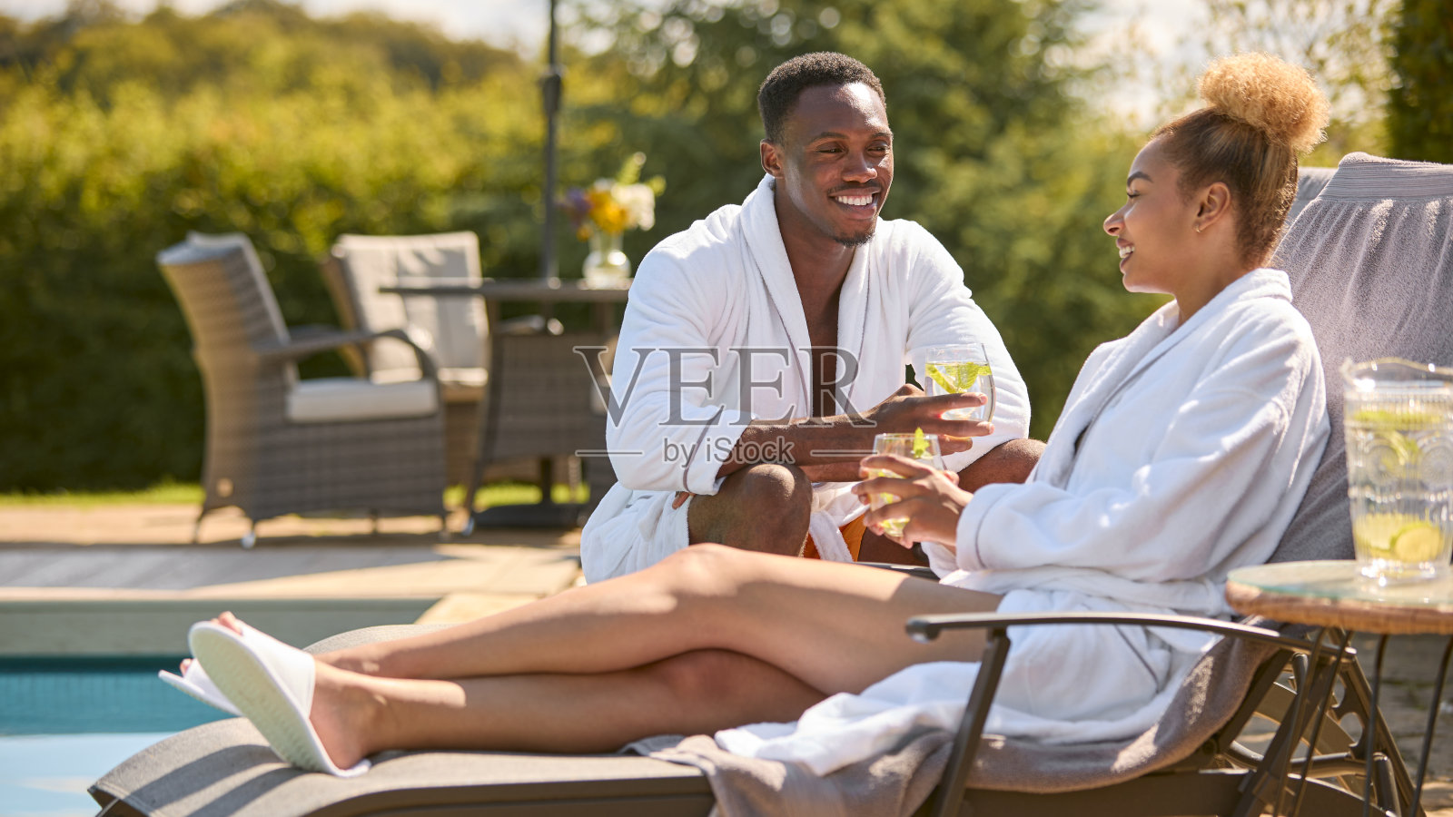 一对夫妇穿着浴袍，坐在泳池边的躺椅上喝着饮料照片摄影图片