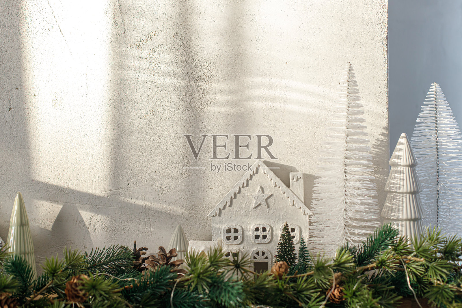 现代圣诞树，房子，松果和云杉树枝在壁炉架上。时尚装饰的圣诞壁炉在最小的斯堪的纳维亚房间在阳光下。本空间照片摄影图片