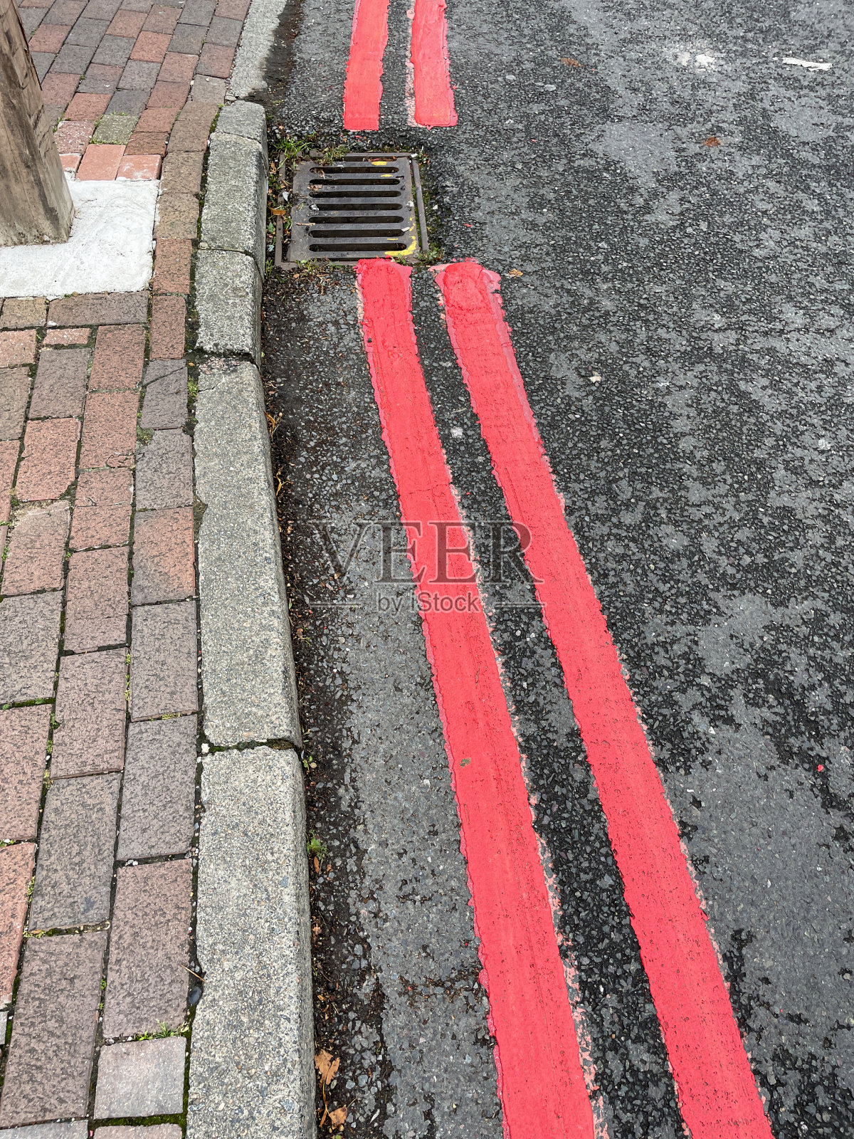 绘制的特写图像，道路排水沟中的双红线，砖路面旁的柏油路路面，红色路线，禁止停车，路边标志，金属格栅，雨水渠，高架视图照片摄影图片