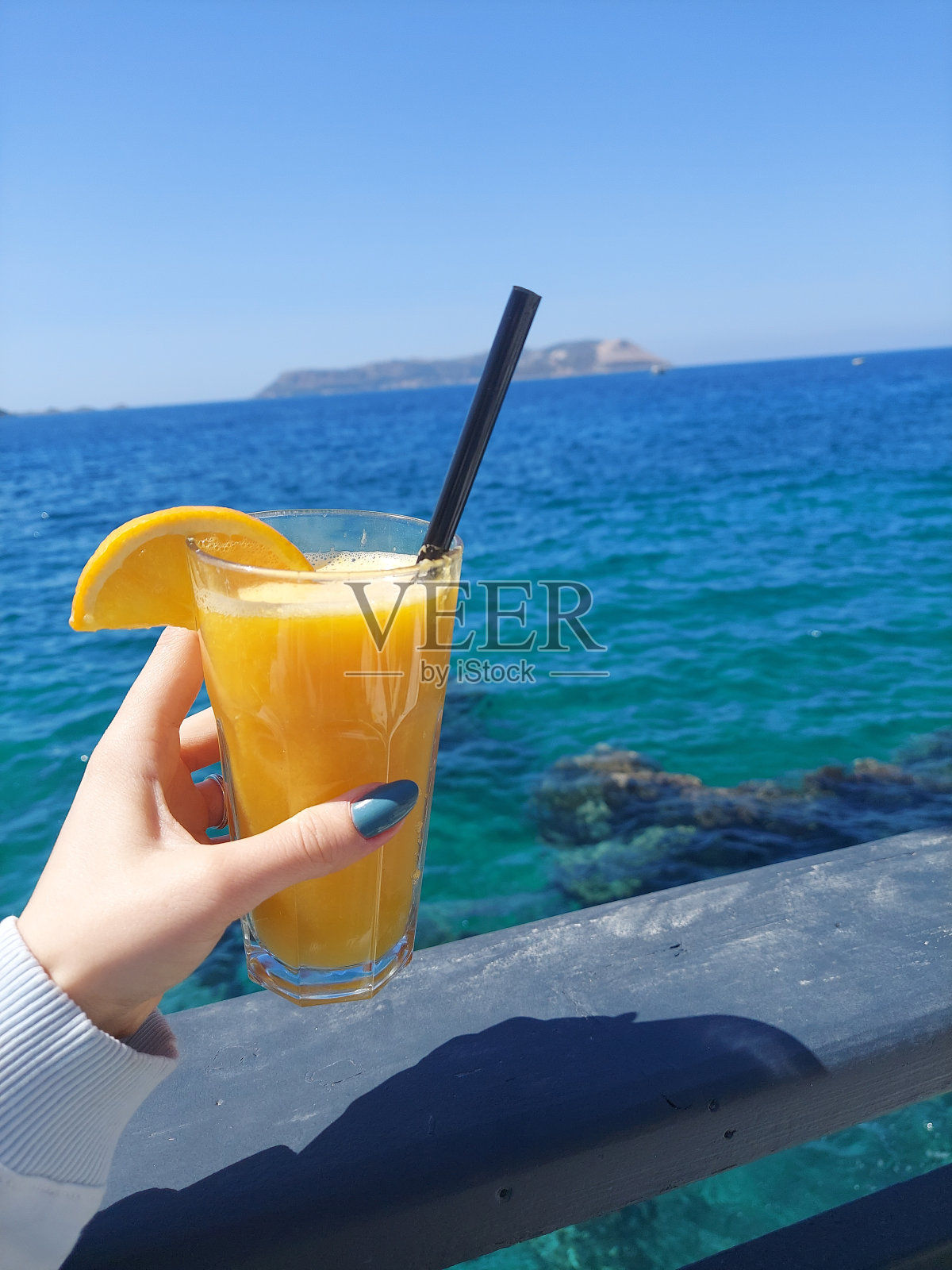 一个女人手里拿着一杯橙汁，背景是大海照片摄影图片