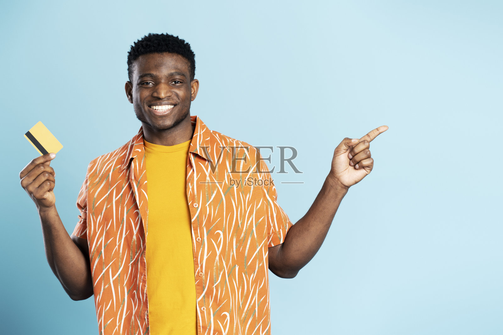 快乐的非裔美国人，拿着信用卡，在蓝色背景下看着相机照片摄影图片