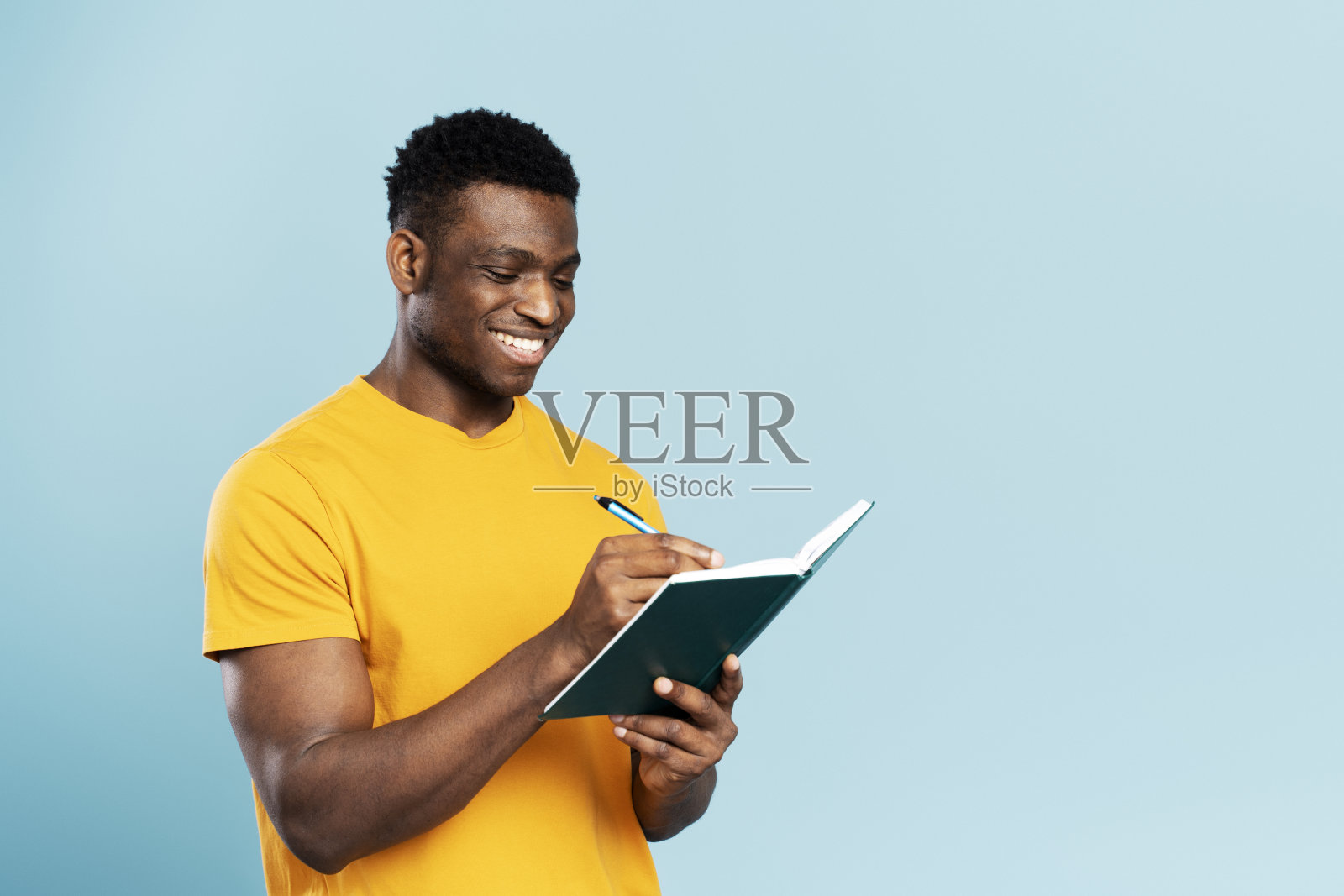 成功作家的肖像微笑着拿着笔记本，在蓝色背景上做笔记照片摄影图片