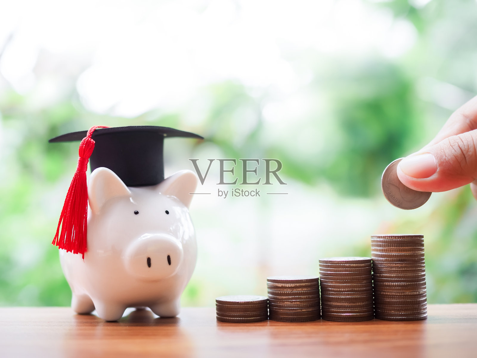 近距离的手把硬币放在一堆硬币和存钱罐与毕业帽。为将来的教育、学生贷款、奖学金、学费存钱的概念照片摄影图片