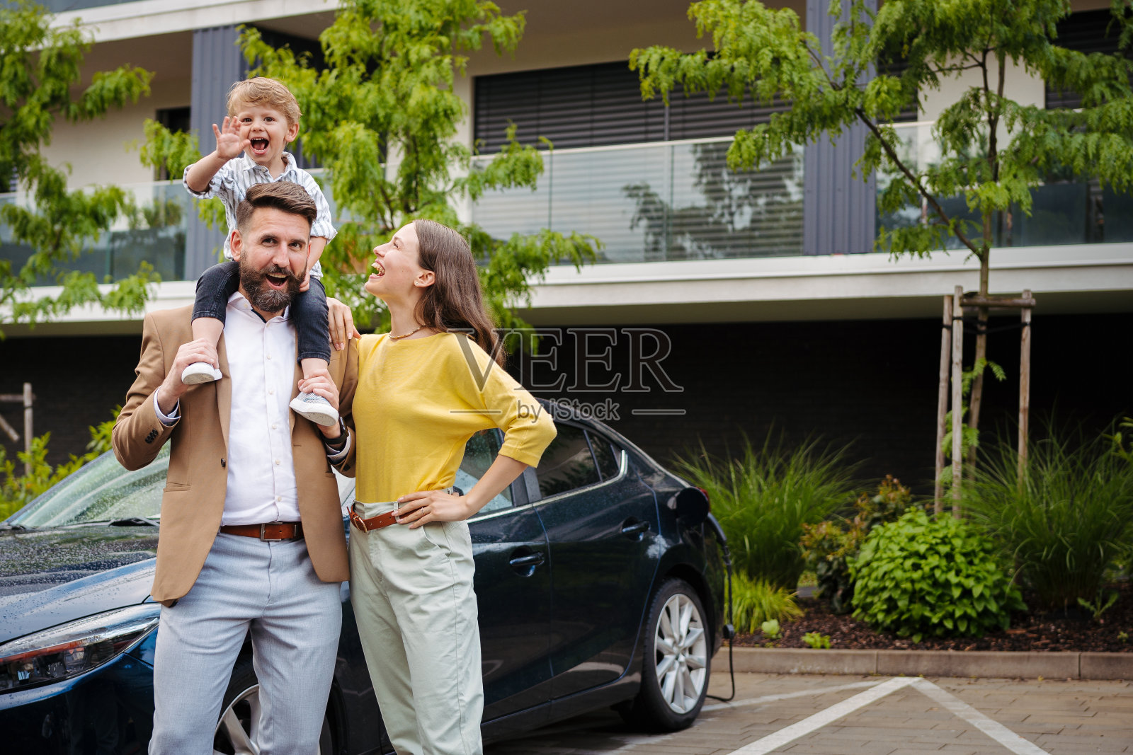 幸福的一家人站在他们的电动车前，在街上给它充电。照片摄影图片