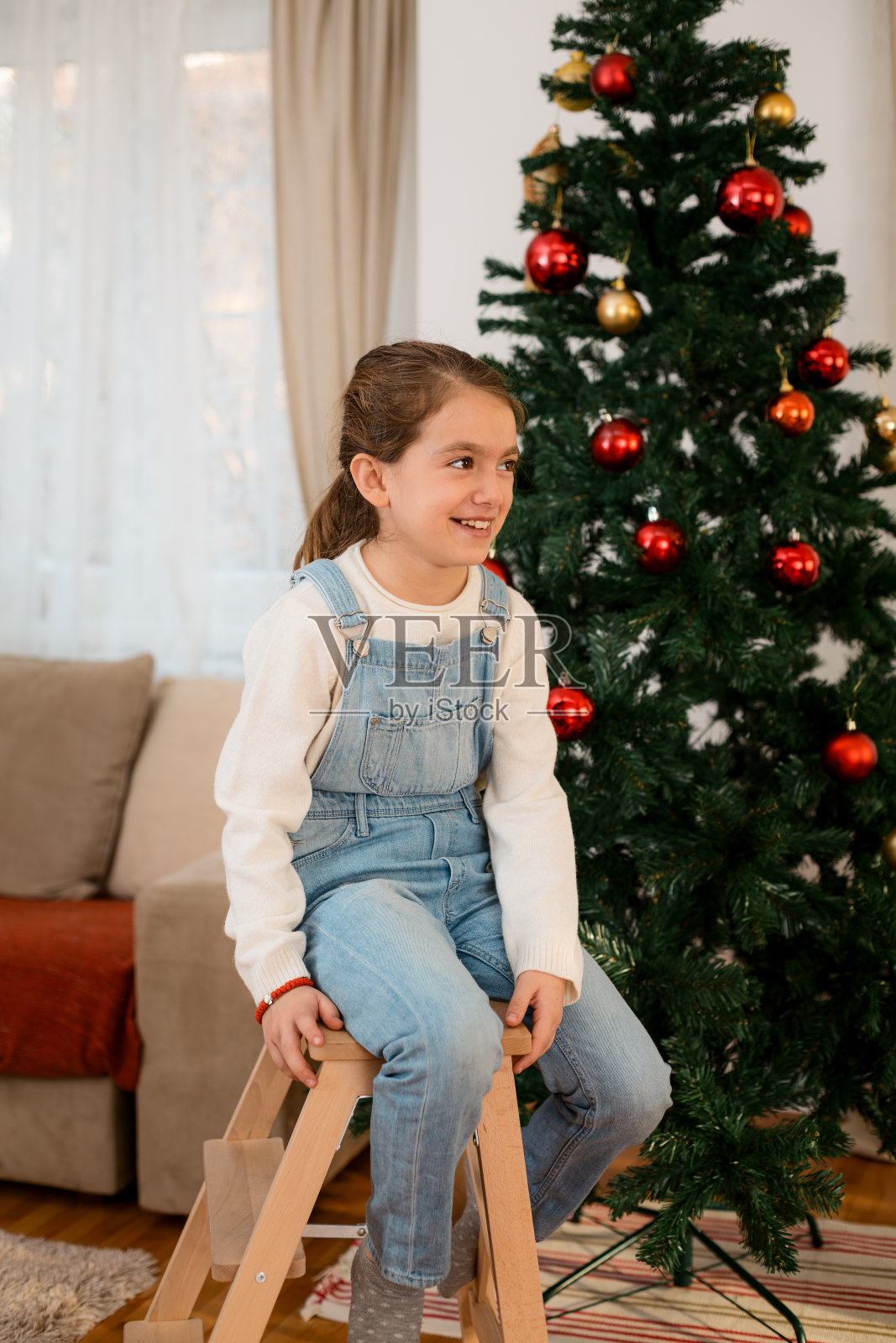 微笑的小女孩坐在圣诞树前的梯子上照片摄影图片