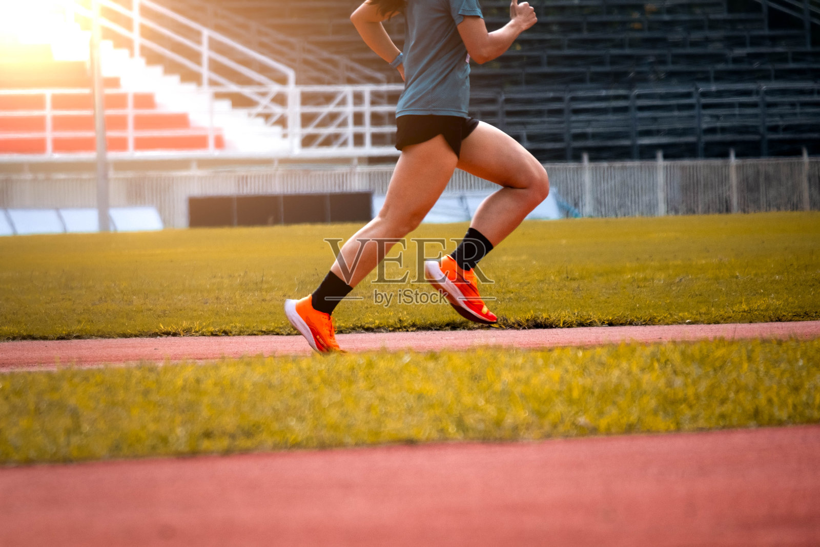 在室外跑道上奔跑的运动员的脚。一个健康的年轻人正在跑道上跑步。穿着运动服的男运动员在室外的体育场跑道上跑着。照片摄影图片