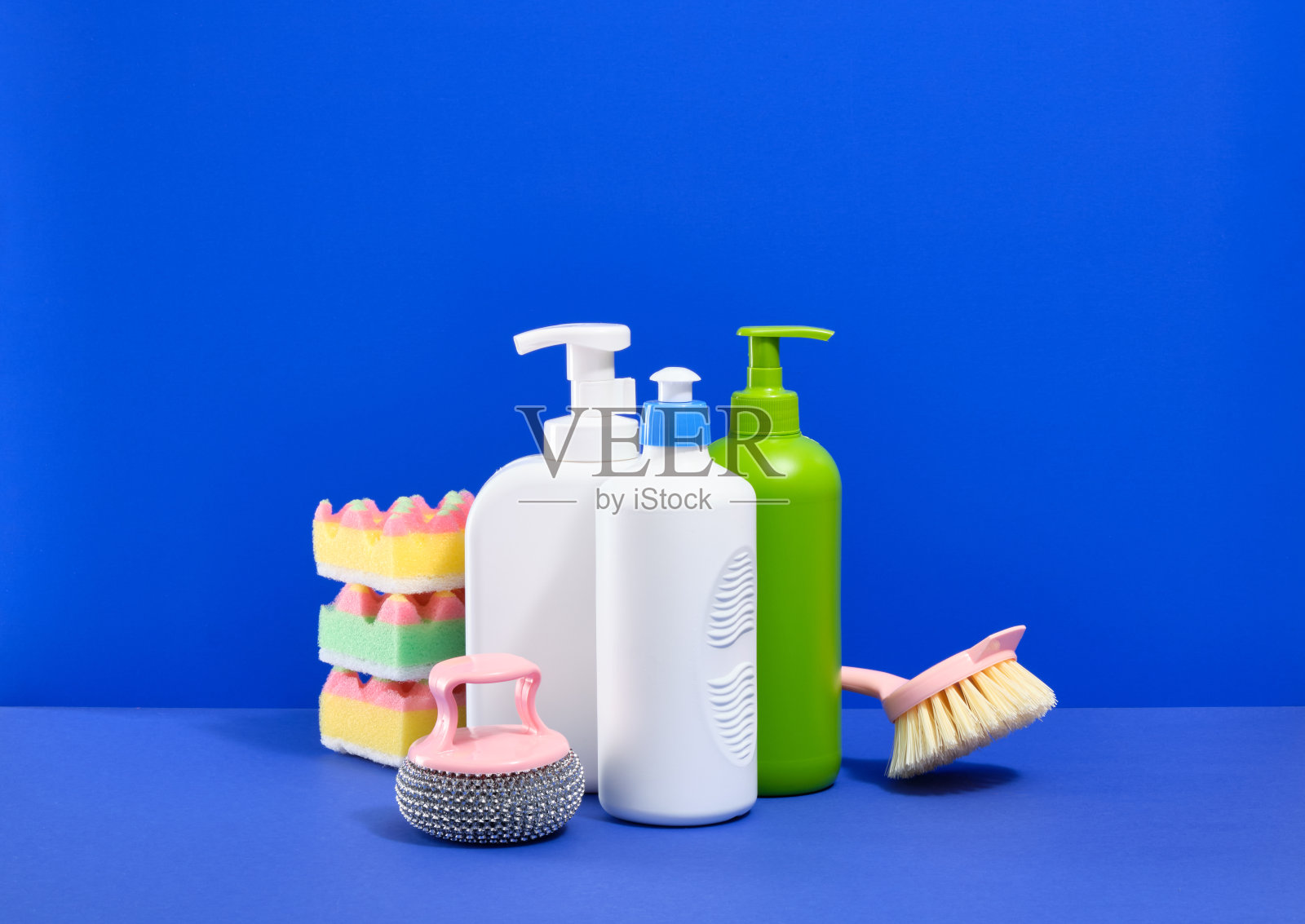 在厨房里洗盘子。海绵，洗碗刷，洗碗清洁剂，蓝色背景。照片摄影图片