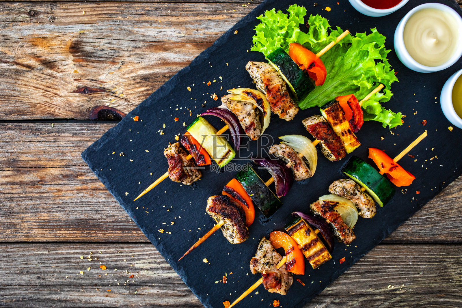 烤肉串——烤肉和蔬菜放在黑木桌上的石盘上照片摄影图片