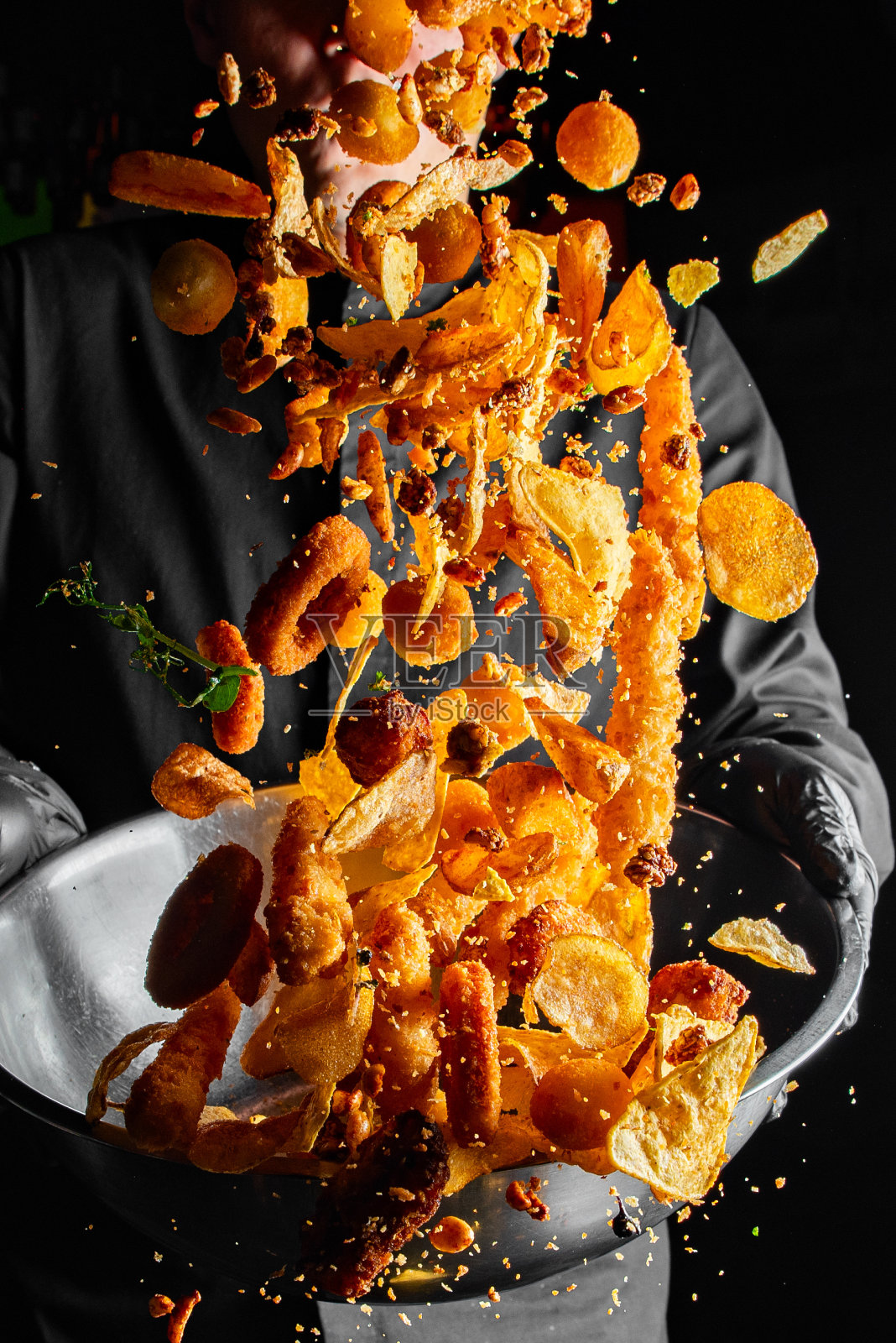 厨师在黑色背景上从碗里扔零食的特写。照片摄影图片